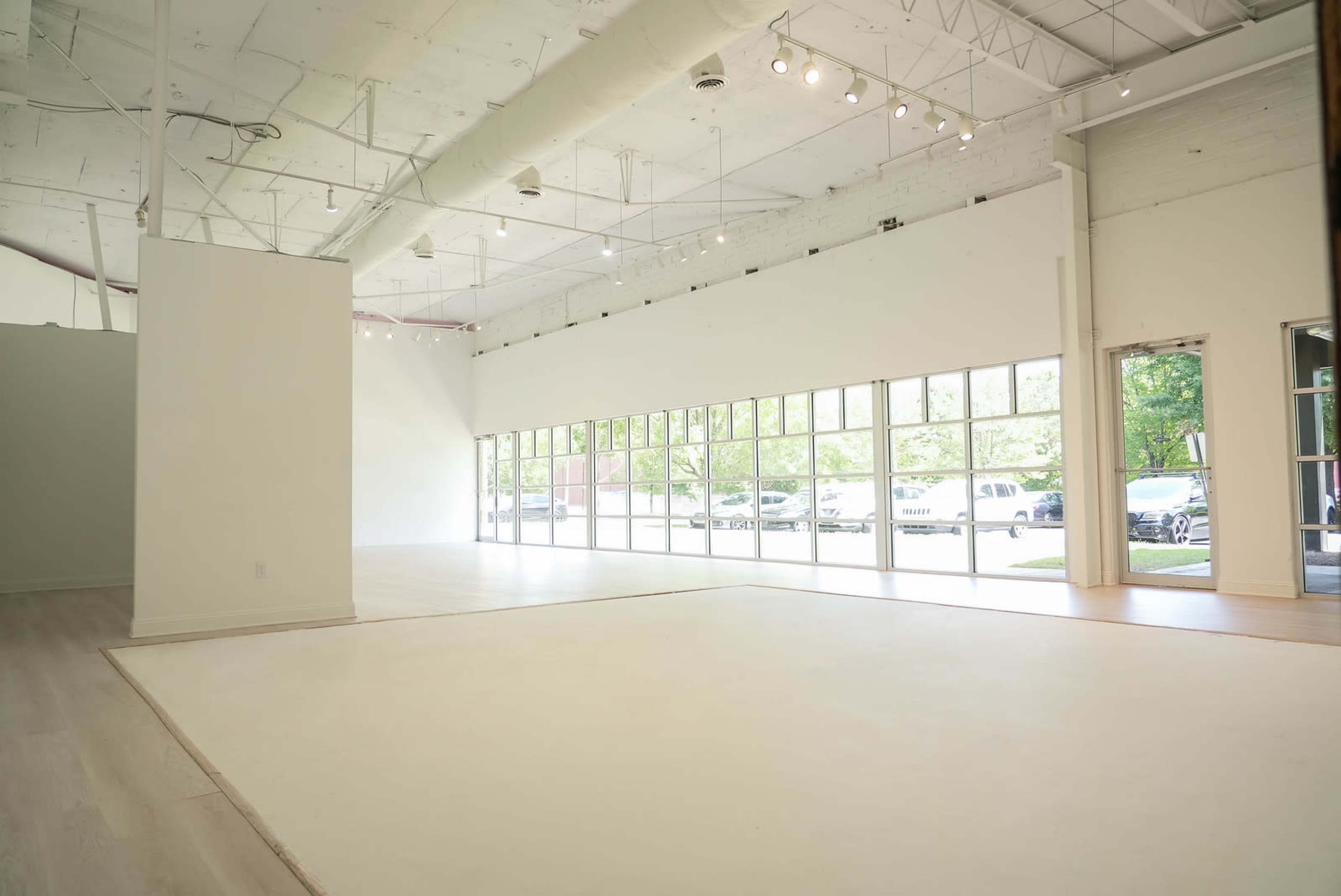 A spacious, well-lit interior of a room with large windows facing an outdoor area and a light-colored floor.