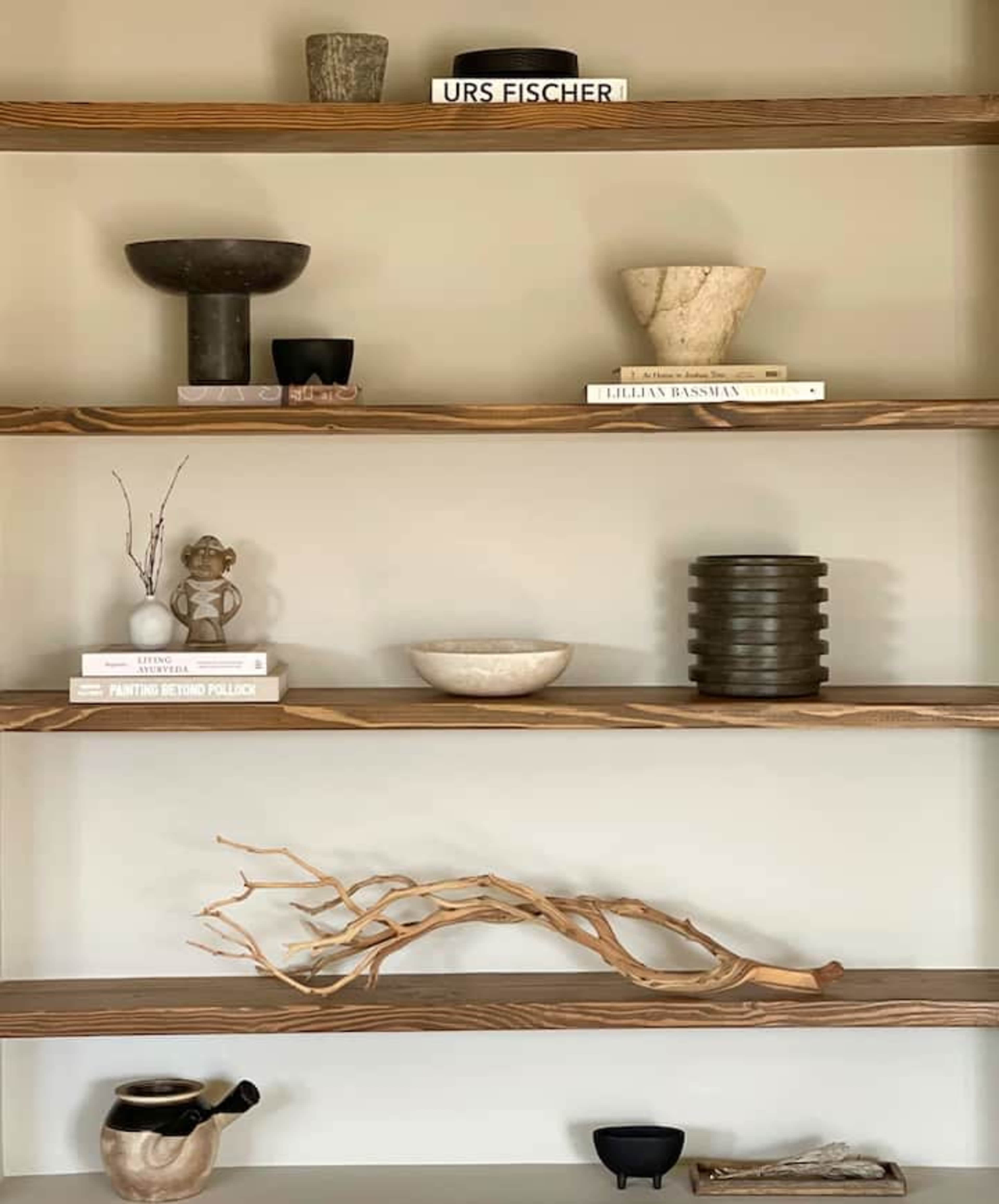 A series of wooden shelves displaying various decorative objects, bowls, and books, along with a piece of driftwood.