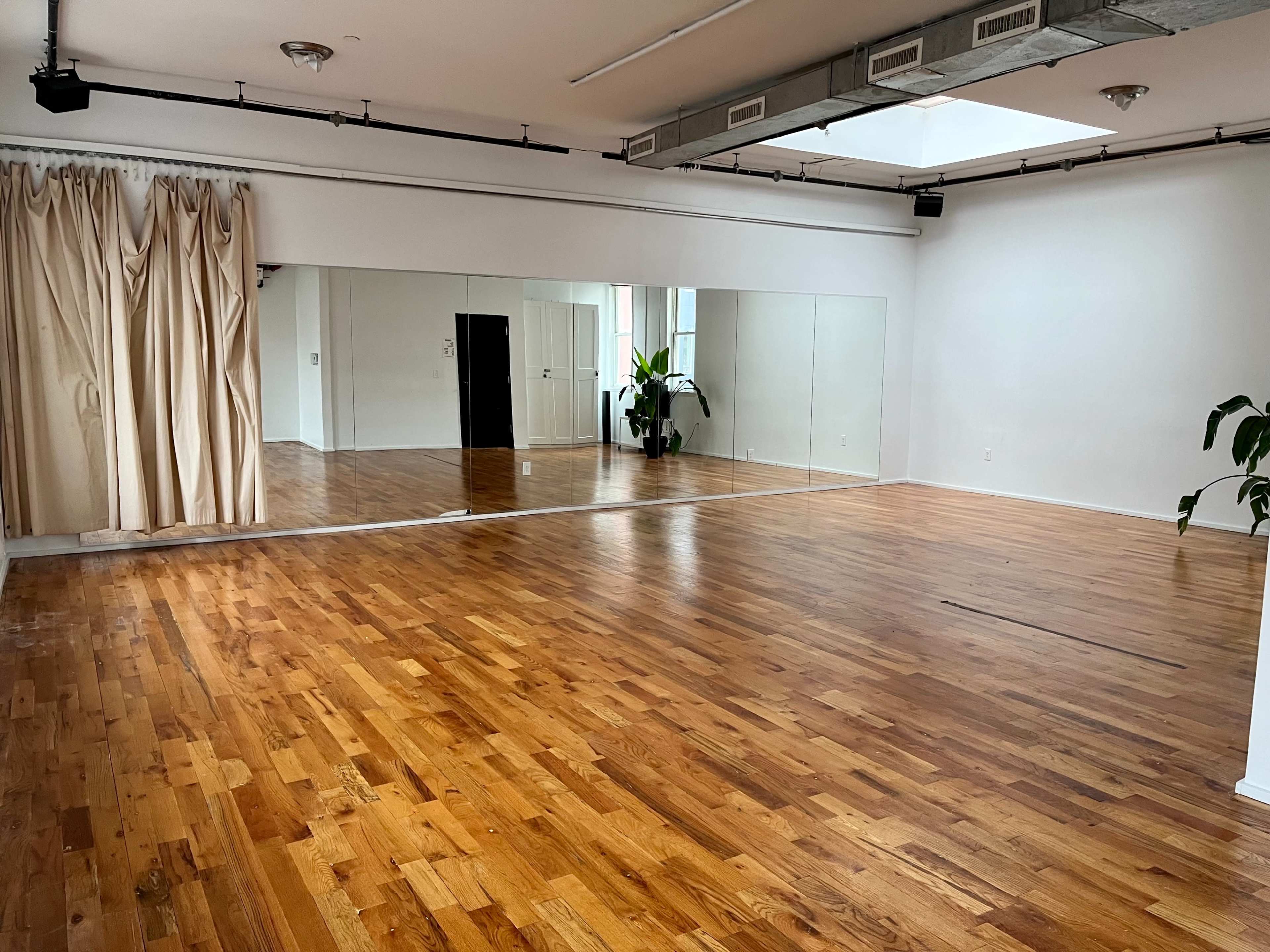 A spacious room with wooden flooring, large mirrors on one wall, and natural light coming from a skylight.
