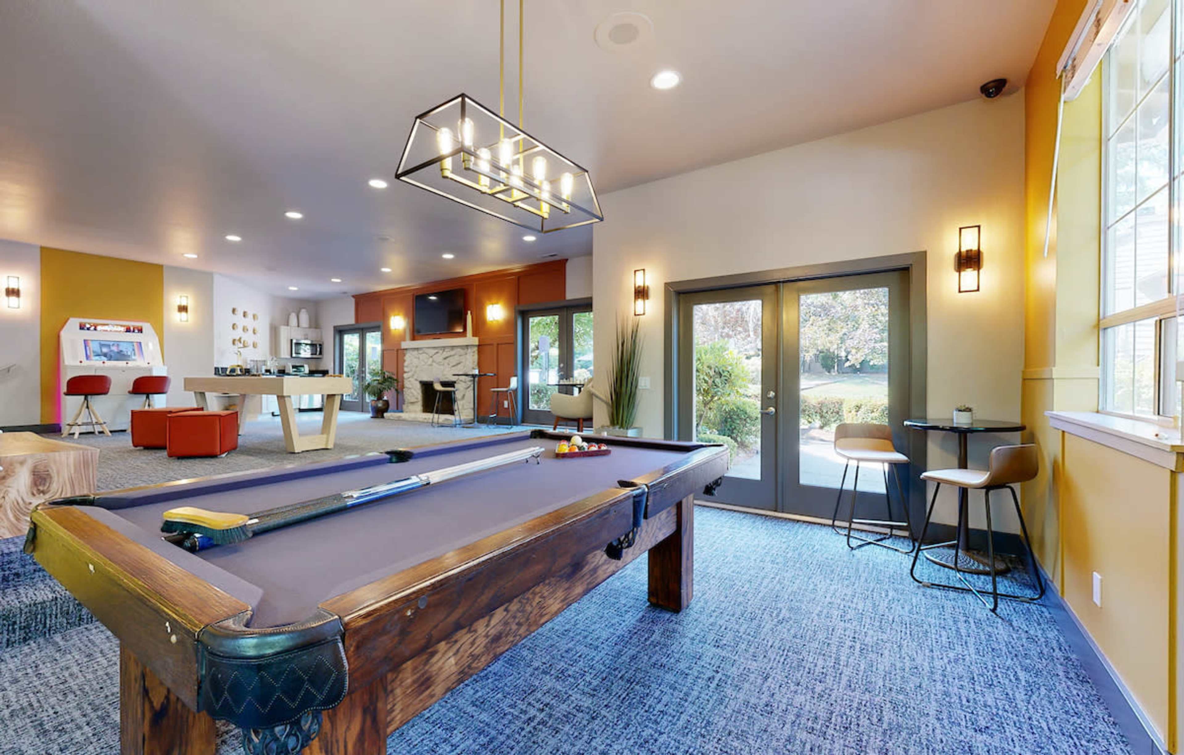 A game room featuring a pool table, seating areas, and large windows that overlook an outdoor space.