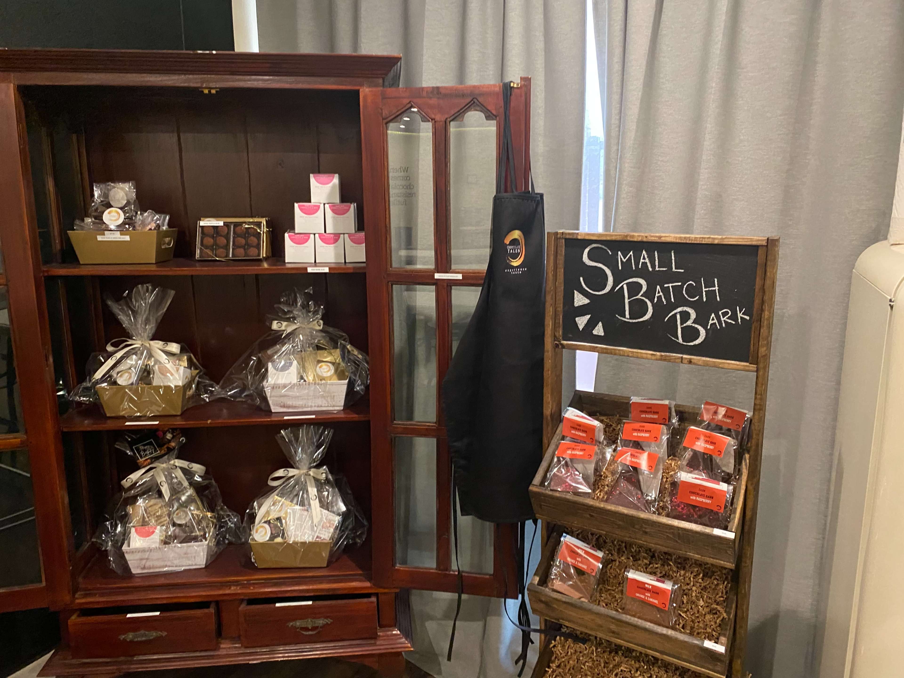 A display featuring an antique wooden cabinet with packaged treats and a sign for "Small Batch Bark" next to a rustic stand holding snack bags.