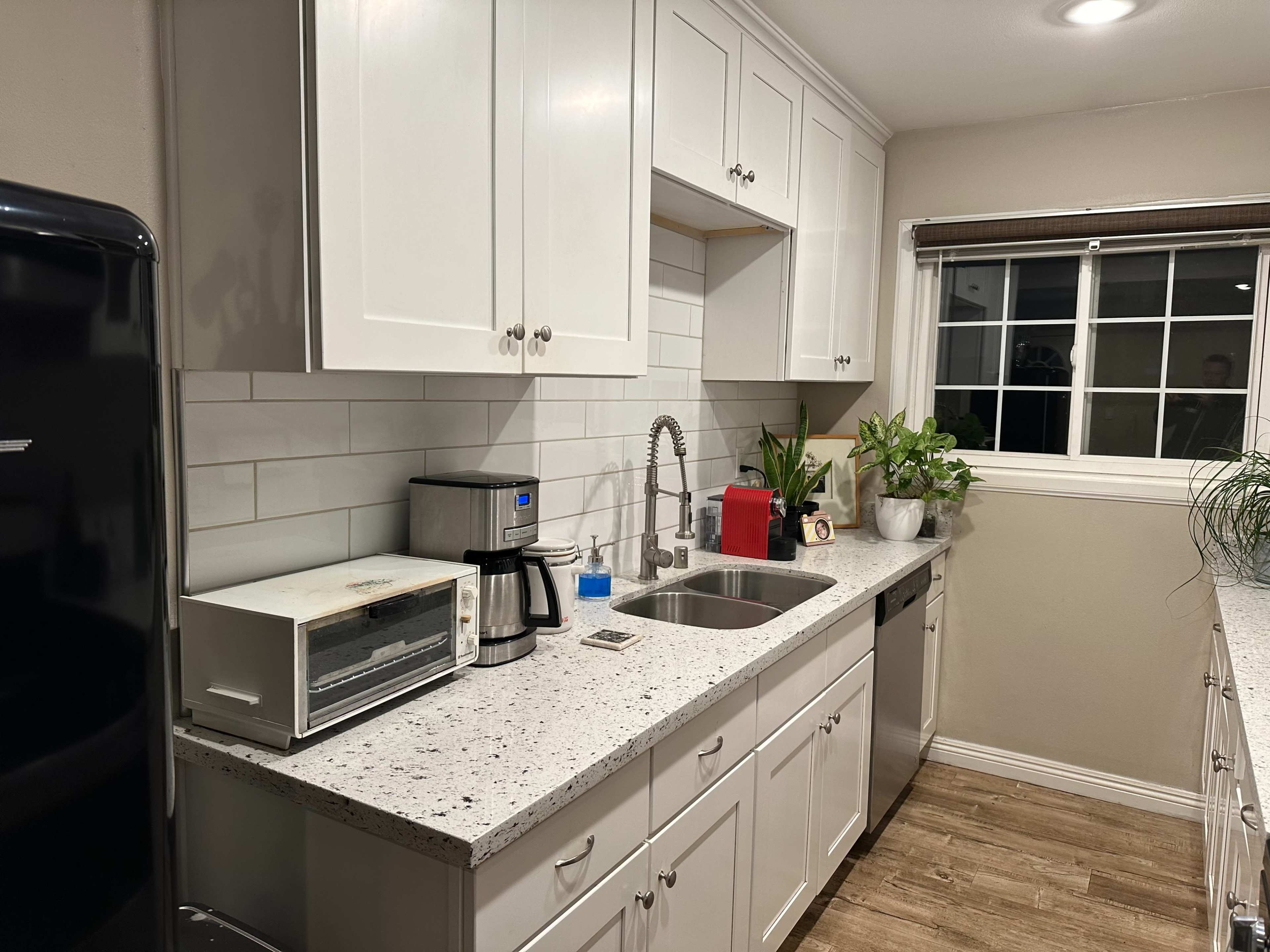 A modern kitchen with white cabinets, a stainless steel sink, and various appliances including a coffee maker and microwave.