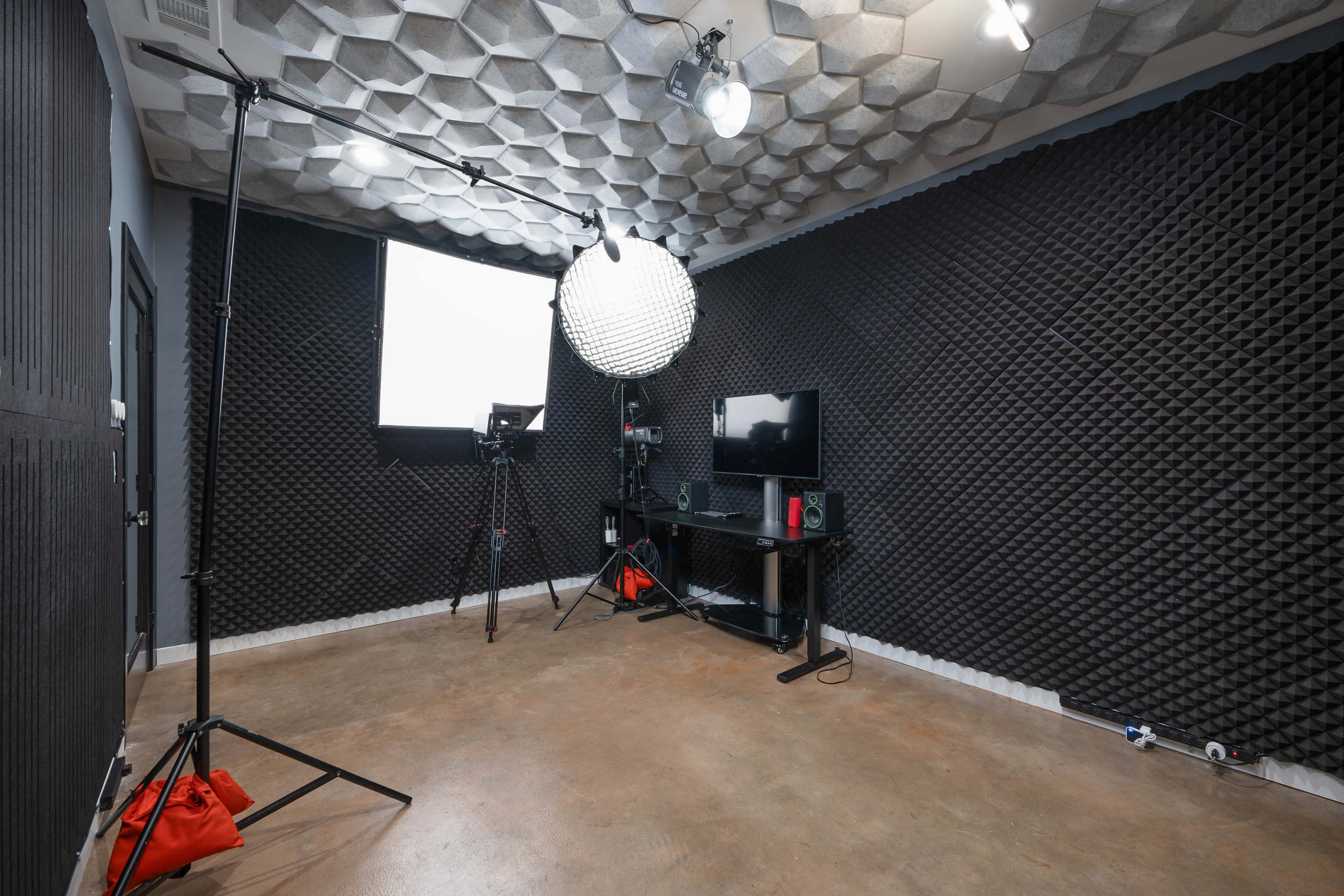 The image shows a soundproofed studio equipped with a lighting setup, camera tripod, and audio equipment arranged around a TV on a black shelf.