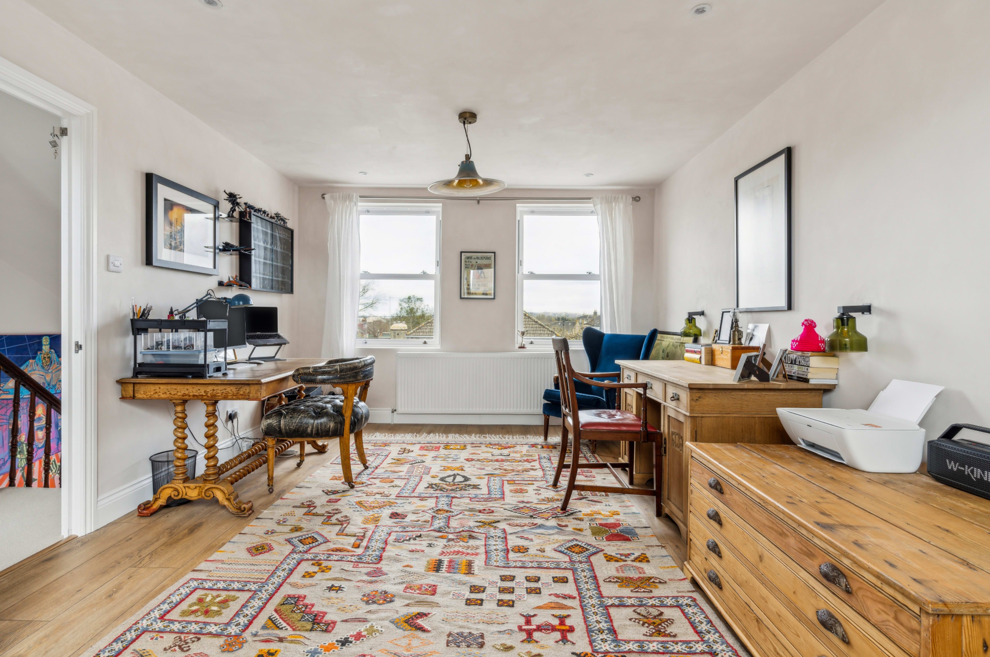 A bright home office with two desks, an area rug, and large windows letting in natural light.