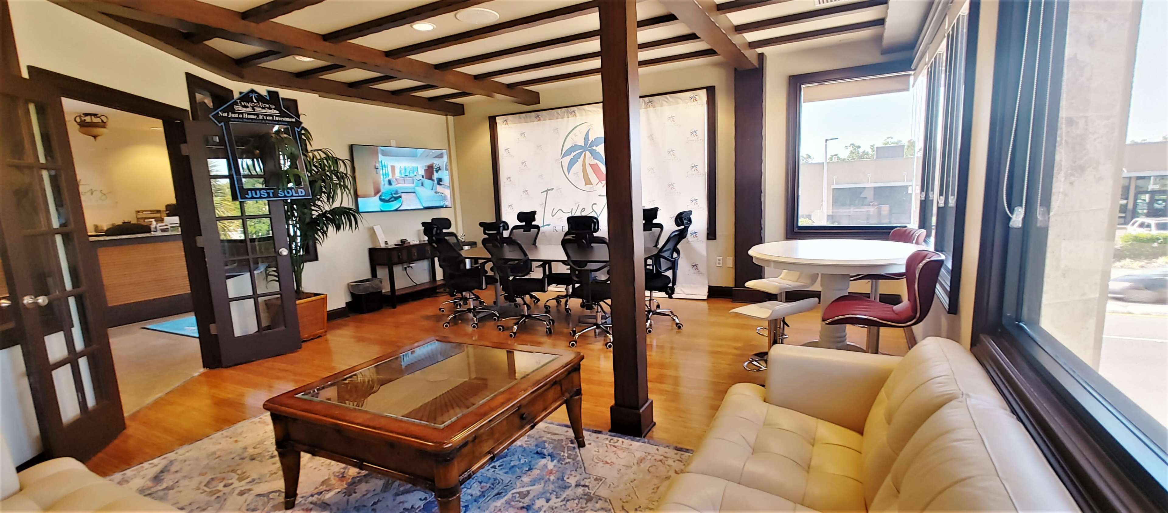 The image depicts a modern office space featuring a conference room with a large table and ergonomic chairs, a reception area with a television, and large windows letting in natural light.