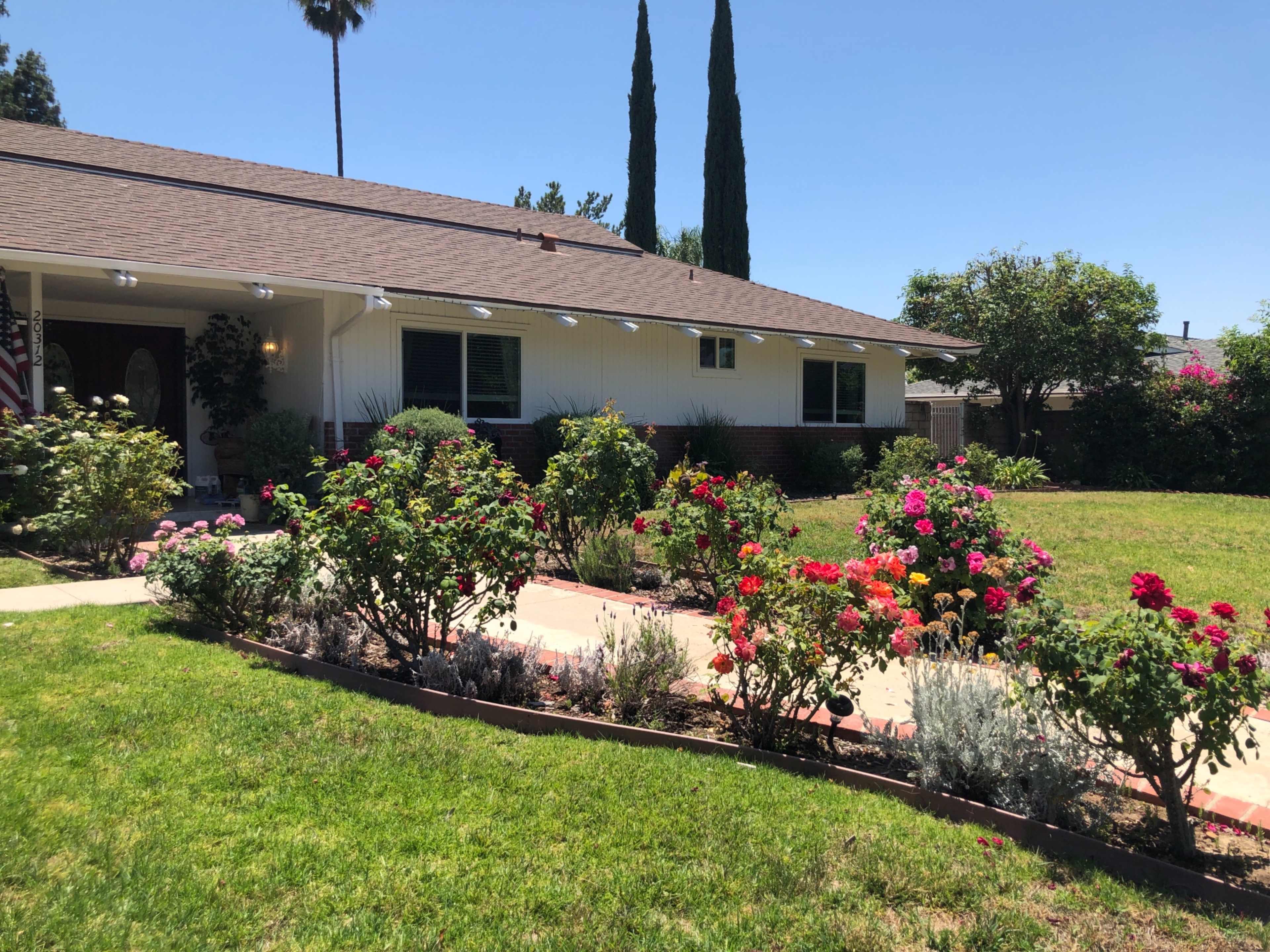 A well-maintained house is surrounded by a colorful garden with blooming flowers and a neatly paved walkway.