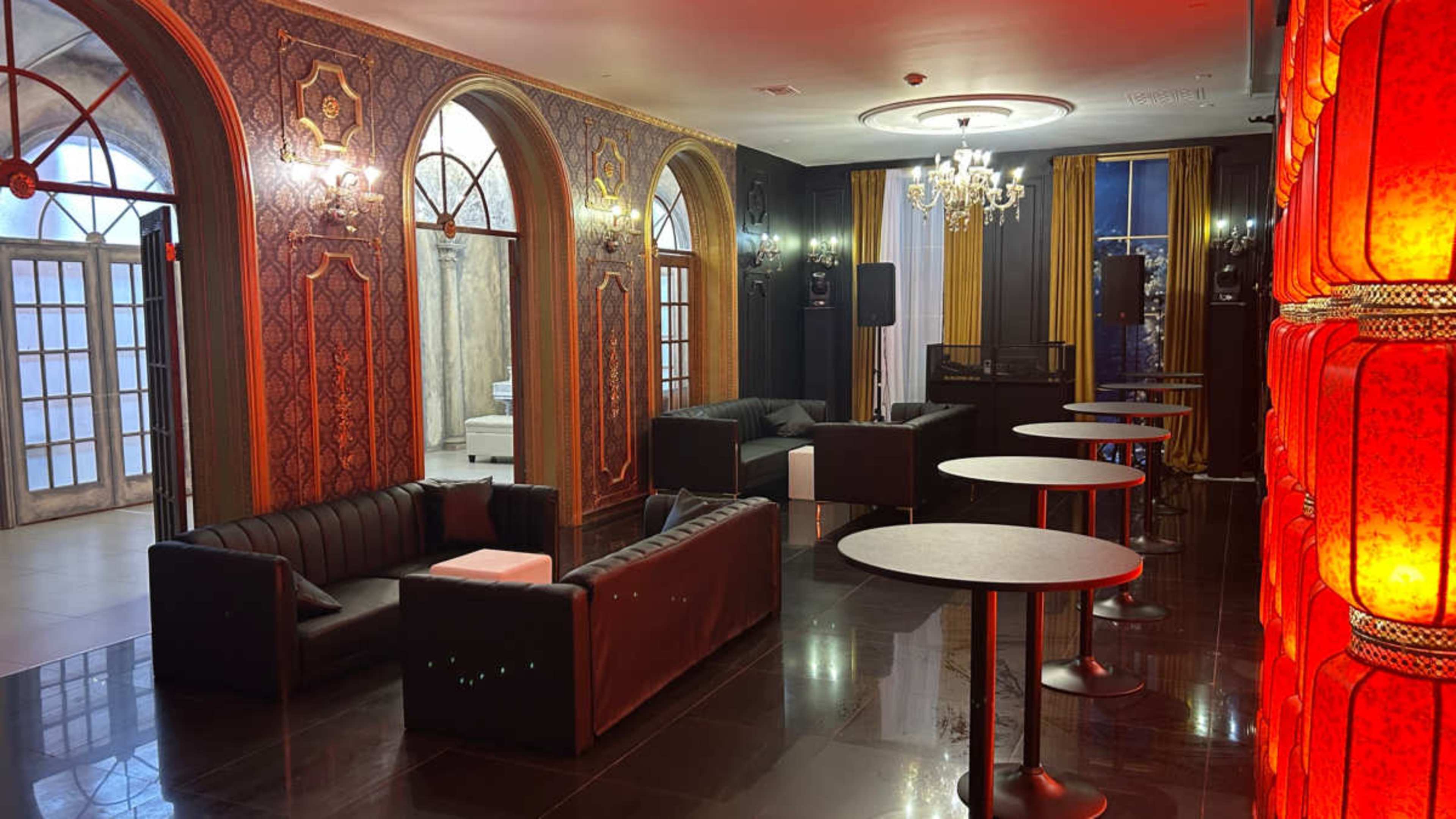 The image shows a modern lounge area with black leather sofas, round tables, and decorative walls featuring ornate designs and warm lighting.