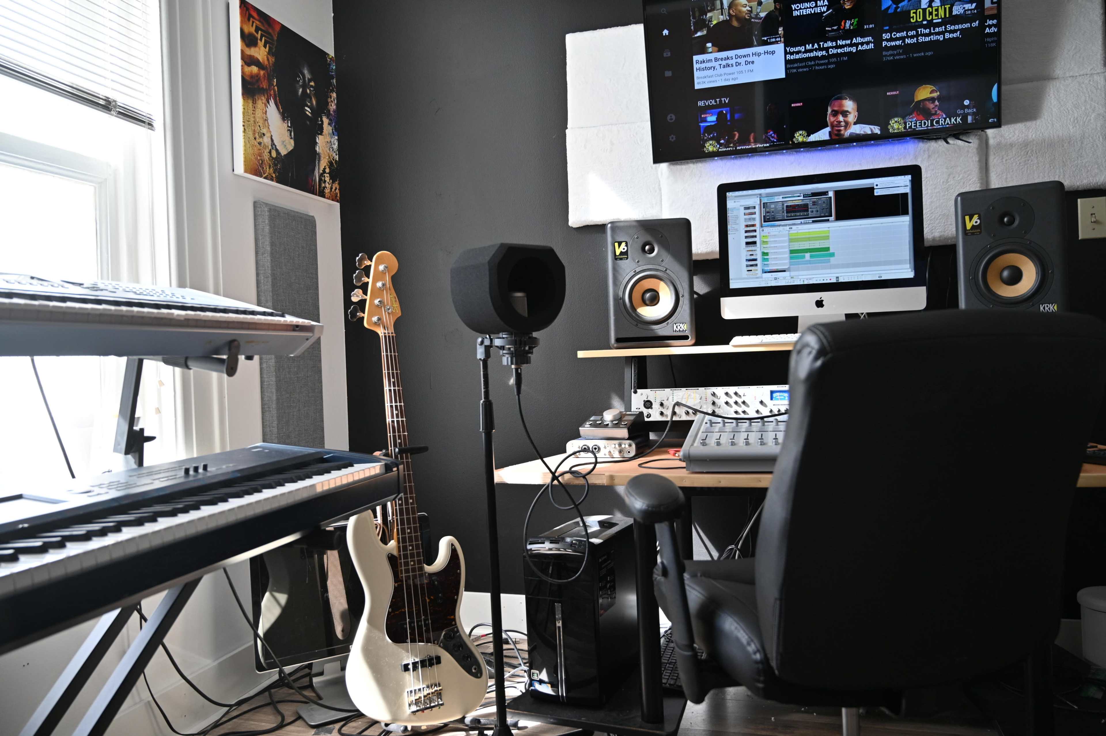 A music production studio features a keyboard, a bass guitar, a computer with recording software, and a microphone setup.