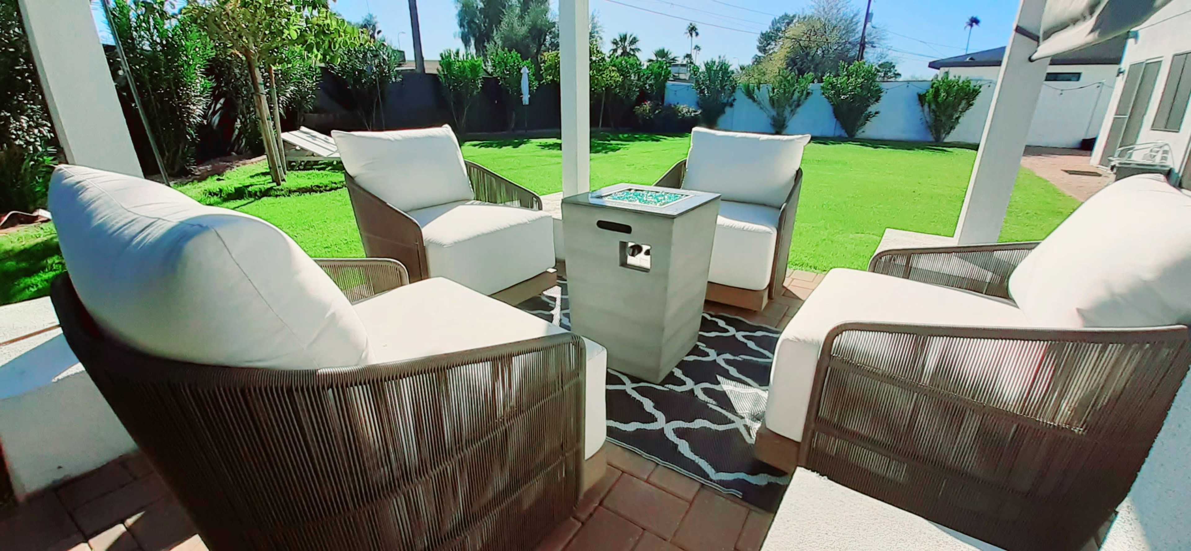 A patio features four cushioned chairs arranged around a small table on a grassy lawn.