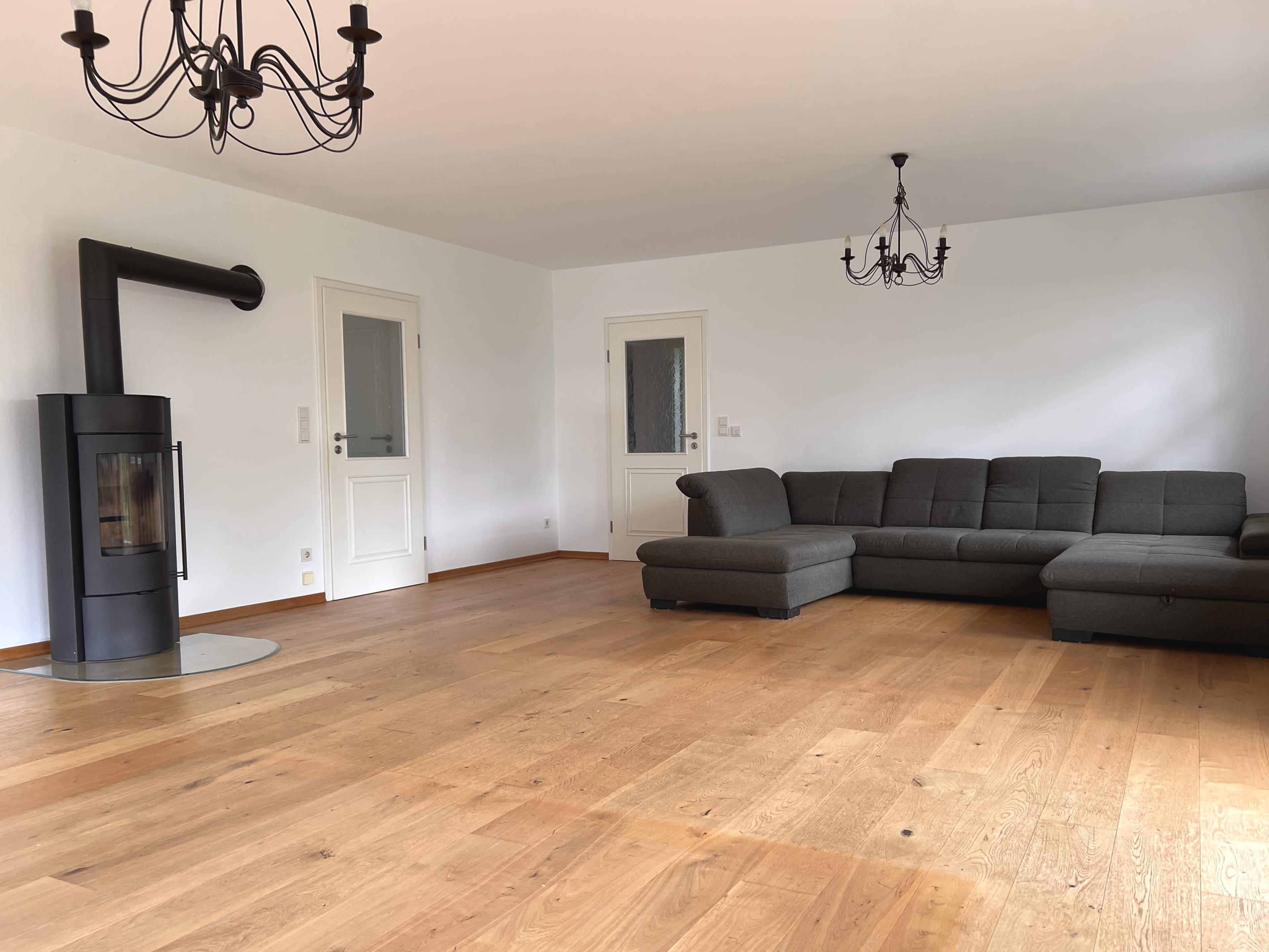 The room features a spacious layout with wooden flooring, a gray sectional sofa, and a modern fireplace.