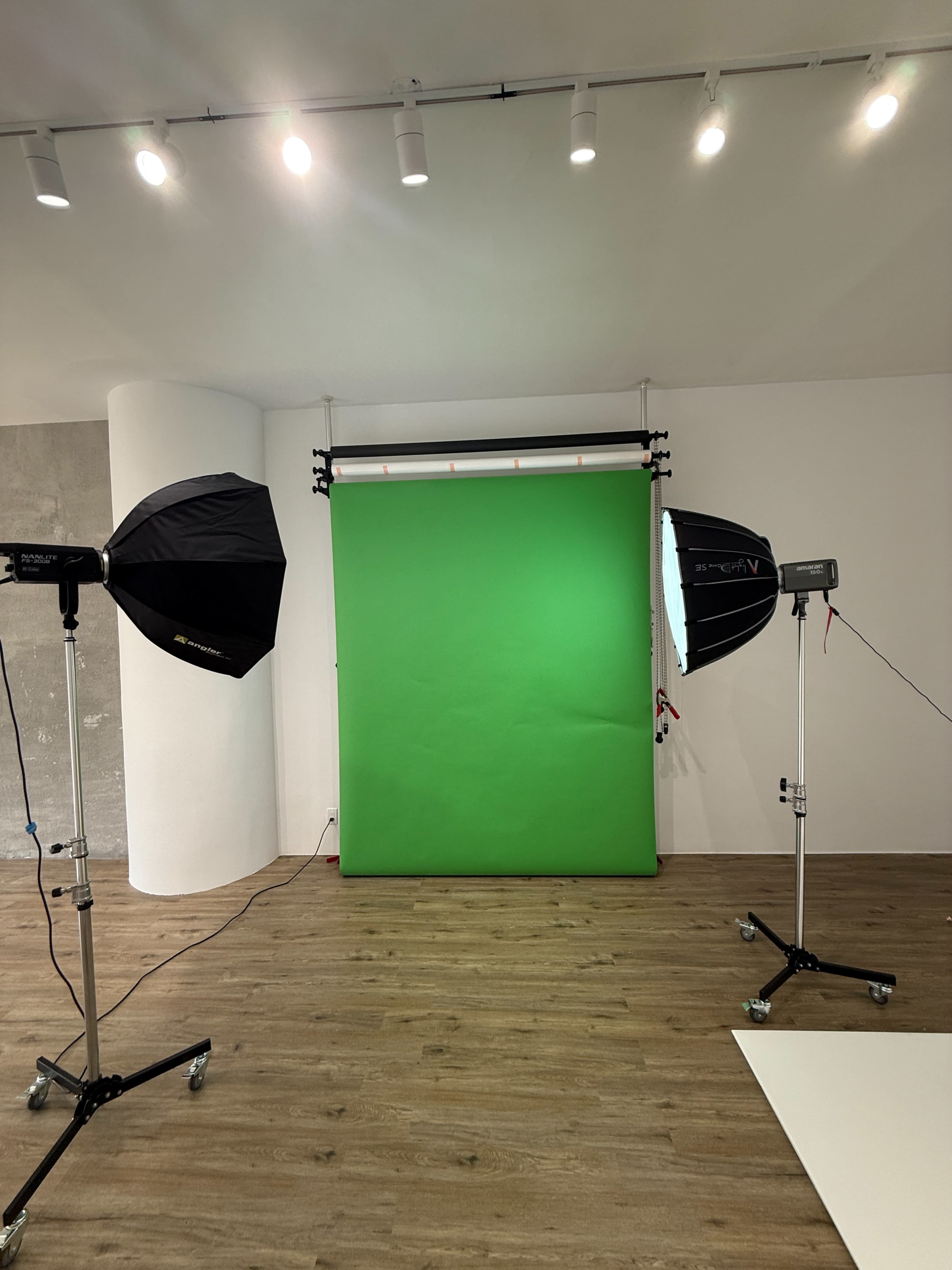 The image shows a photography studio setup with a green backdrop, two studio lights, and wooden flooring.