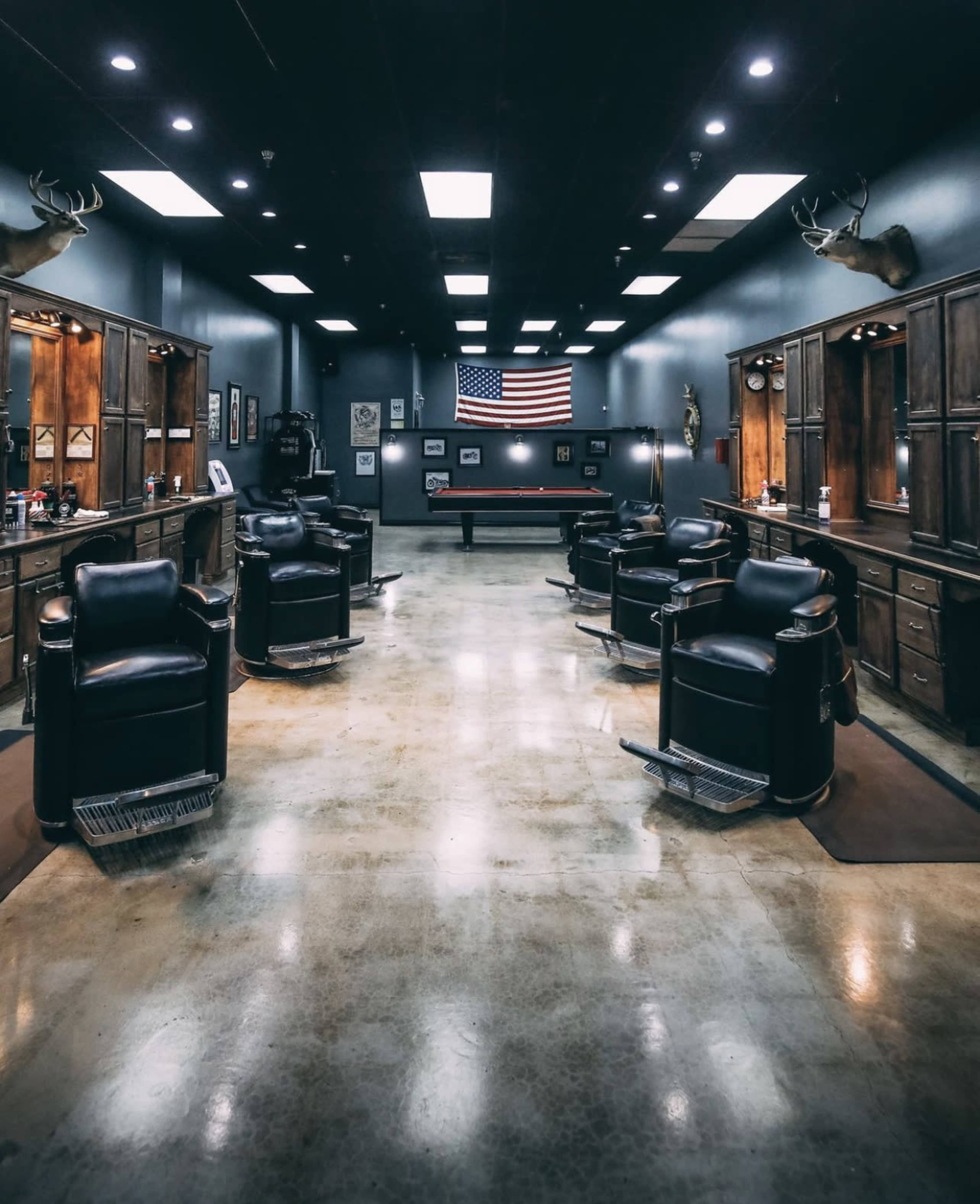 The interior of a barber shop features several black leather chairs arranged in a symmetrical layout, with a large American flag hanging on the back wall.