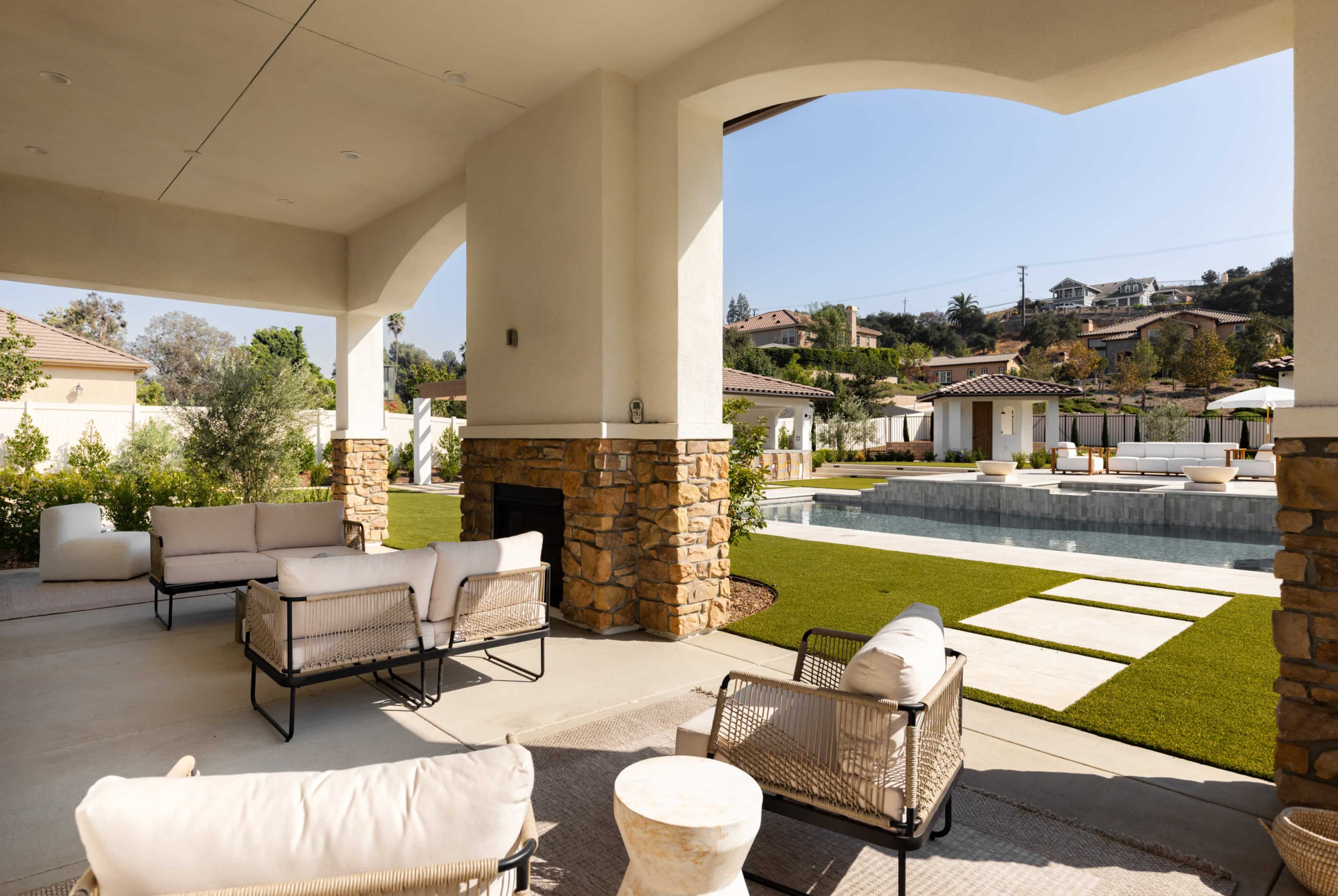 A spacious outdoor seating area features modern furniture and a view of a landscaped pool and garden.