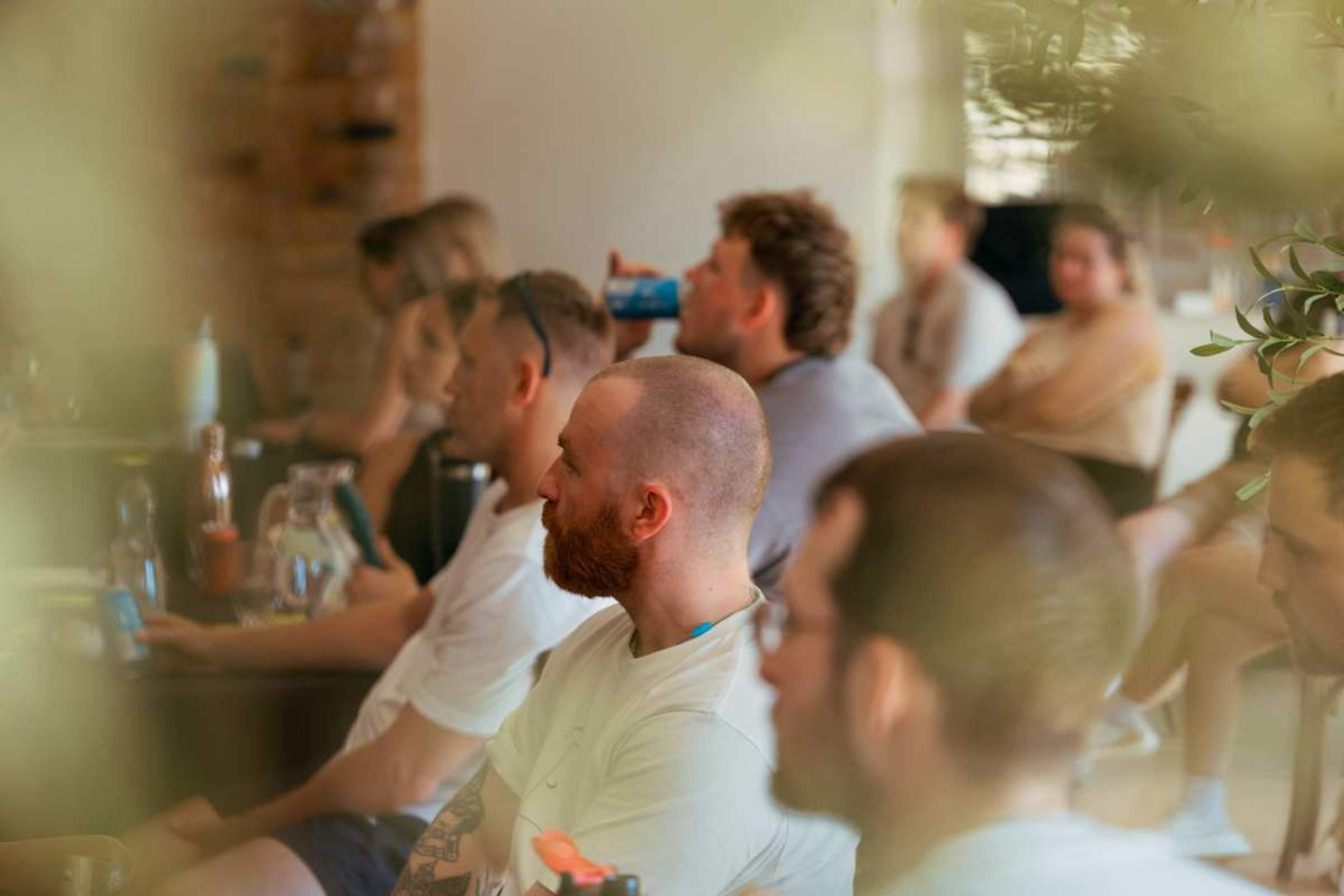 A group of individuals is seated in a casual setting, attentively listening to a speaker or presentation.