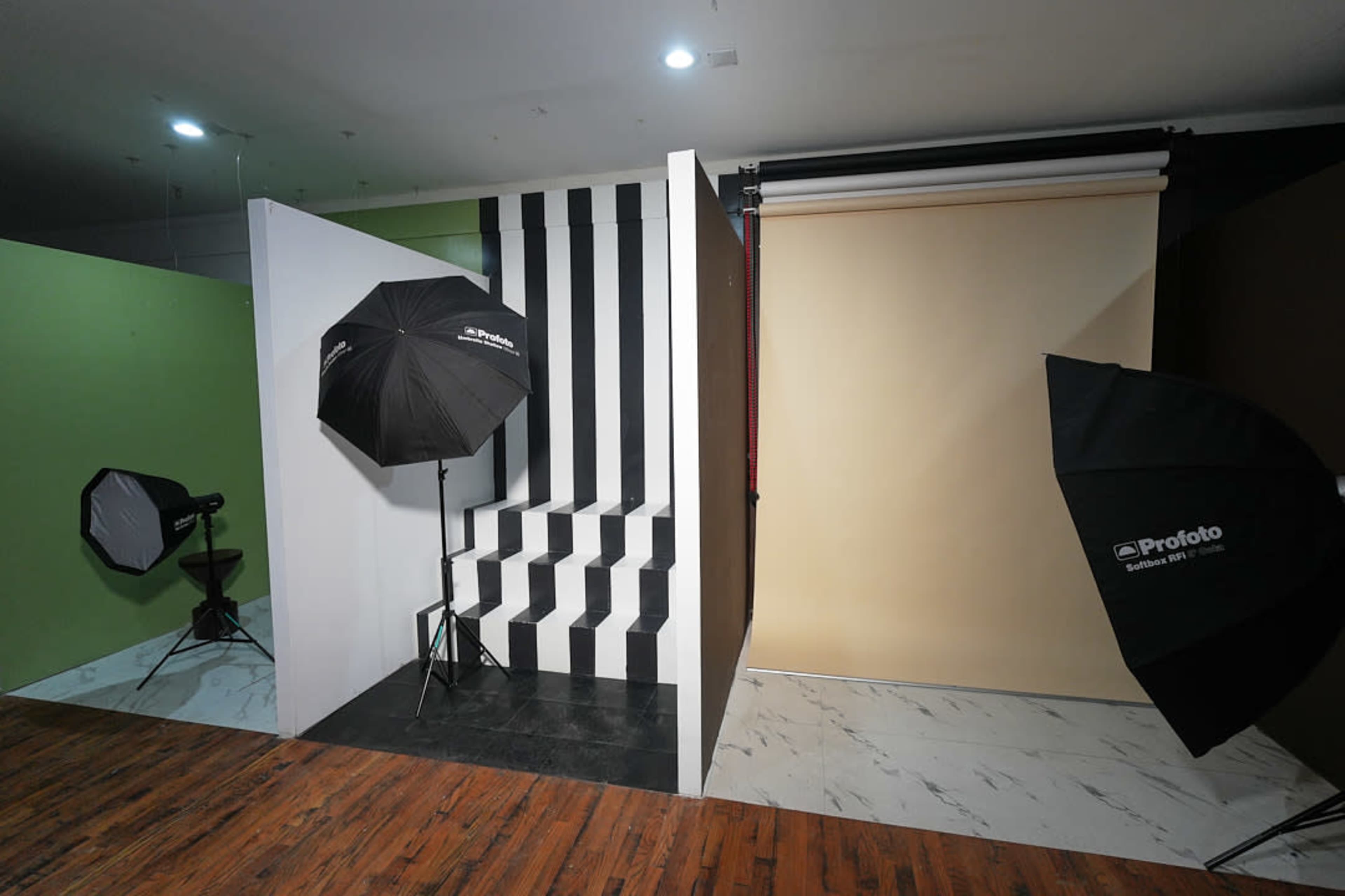 The image shows a photography studio setup with contrasting backdrops, lighting equipment, and a staircase.