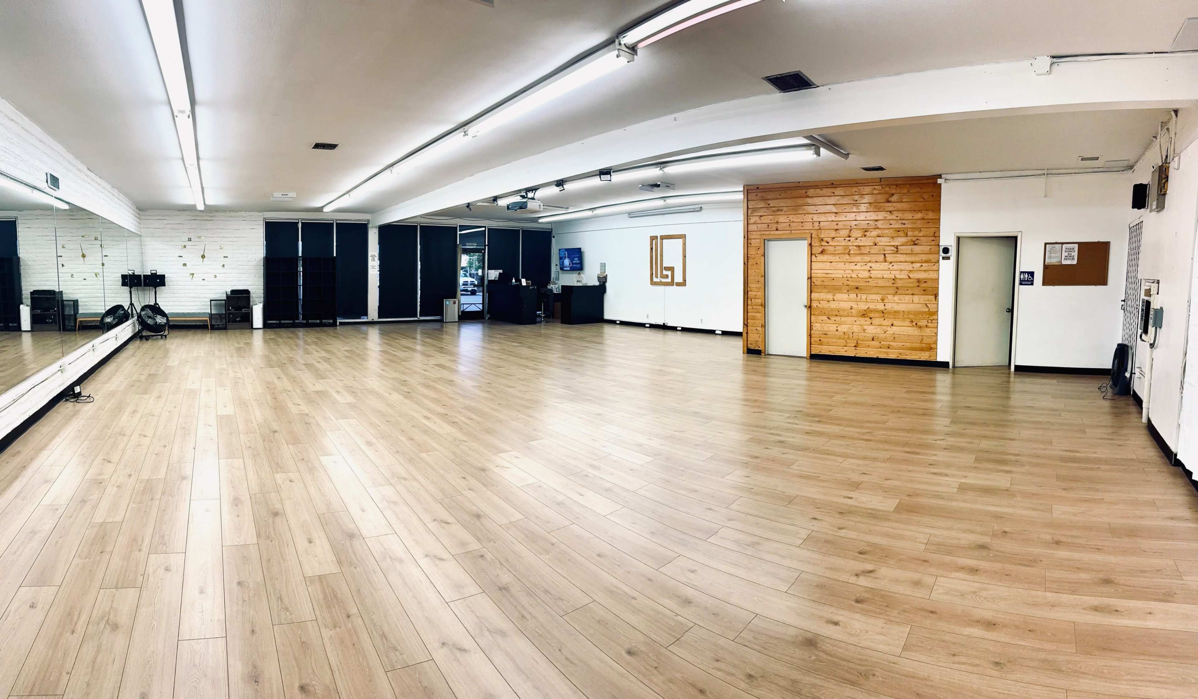 The image shows a spacious dance studio with wooden flooring, large mirrors along one wall, and a wooden accent wall on the opposite side.