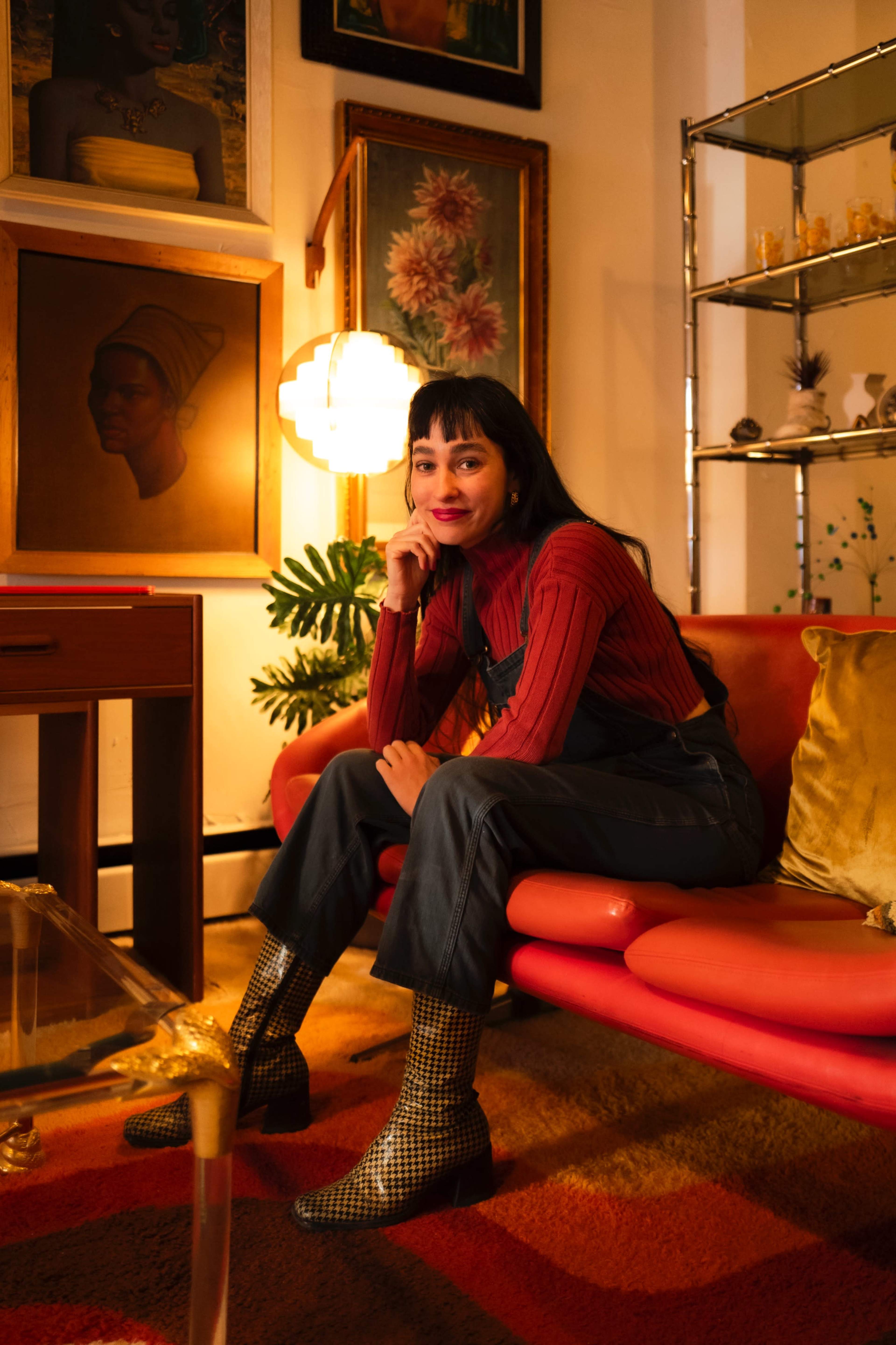 A woman sits on a red sofa in a stylish living room adorned with framed artwork and decorative shelves.