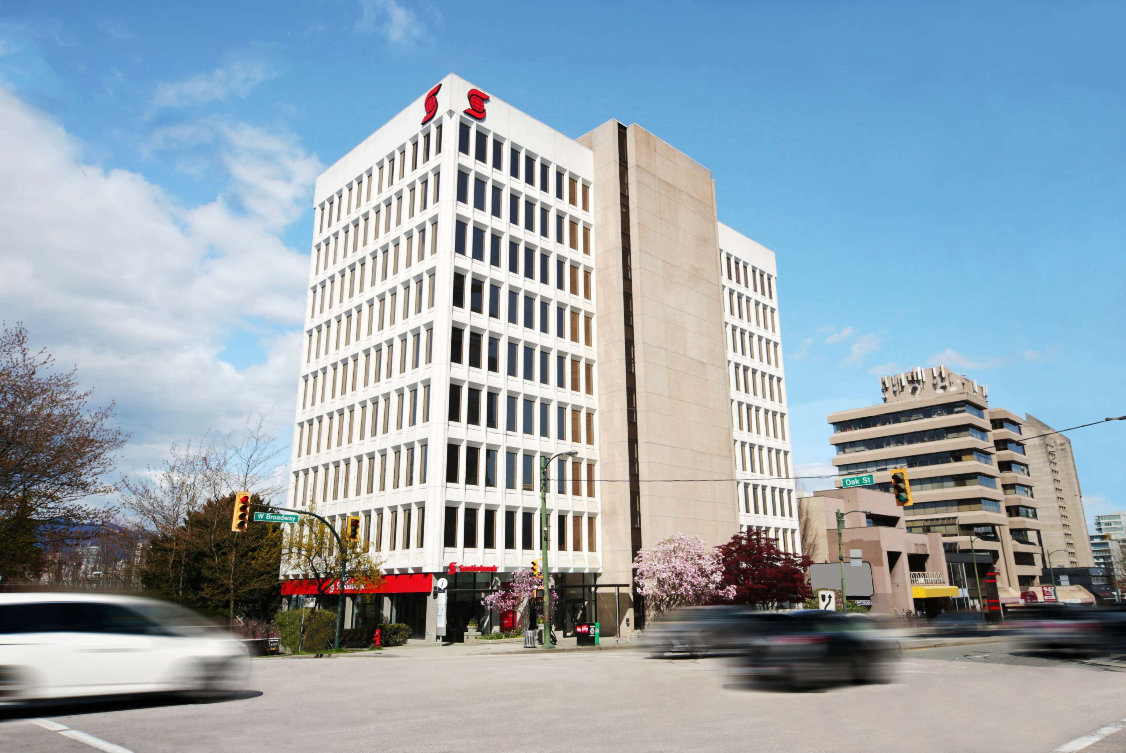 A multi-story office building with a large "S" sign is situated at an urban intersection, surrounded by trees and traffic.