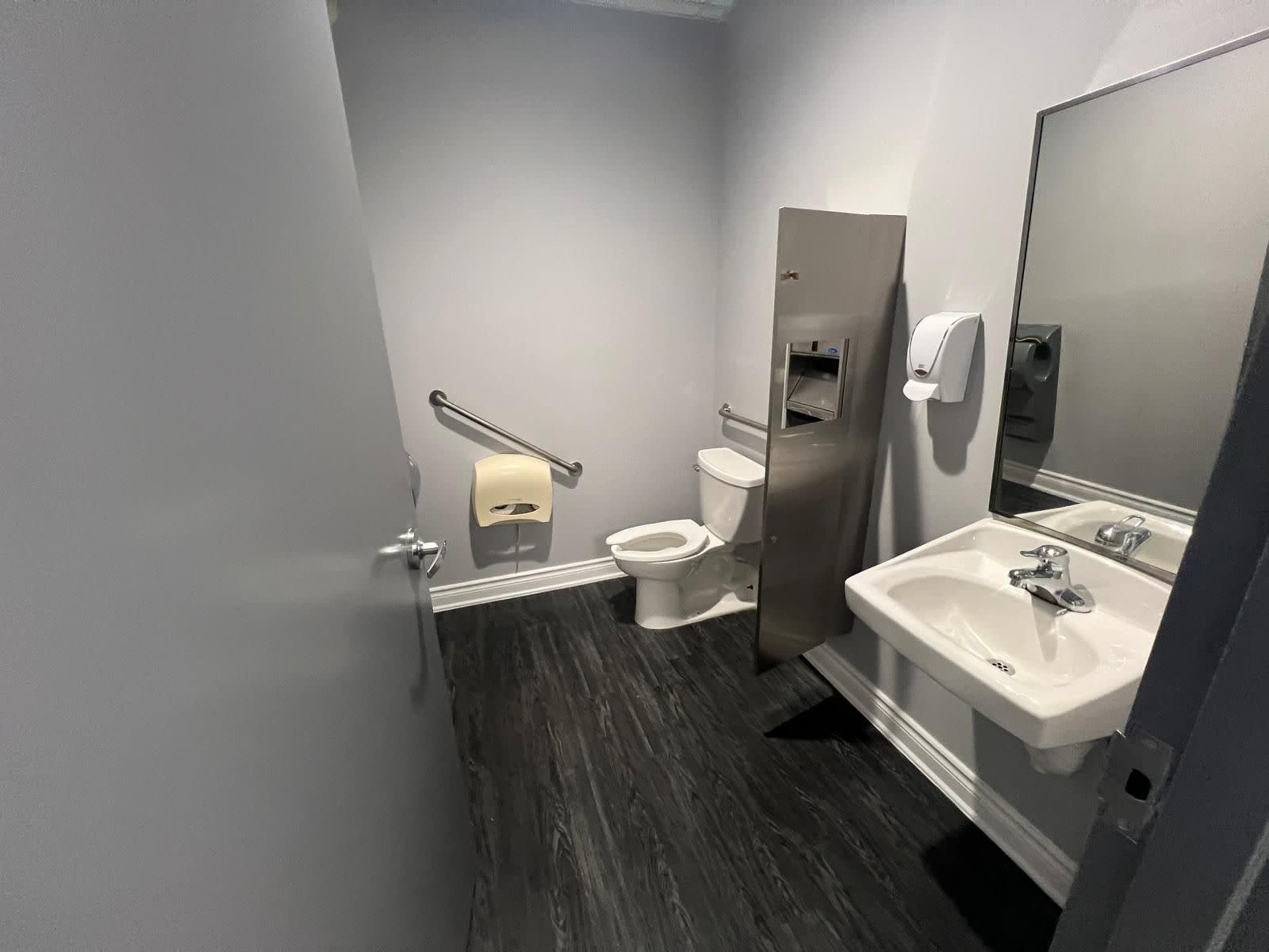 A small restroom with a toilet, sink, and hand sanitizer dispenser on the wall.