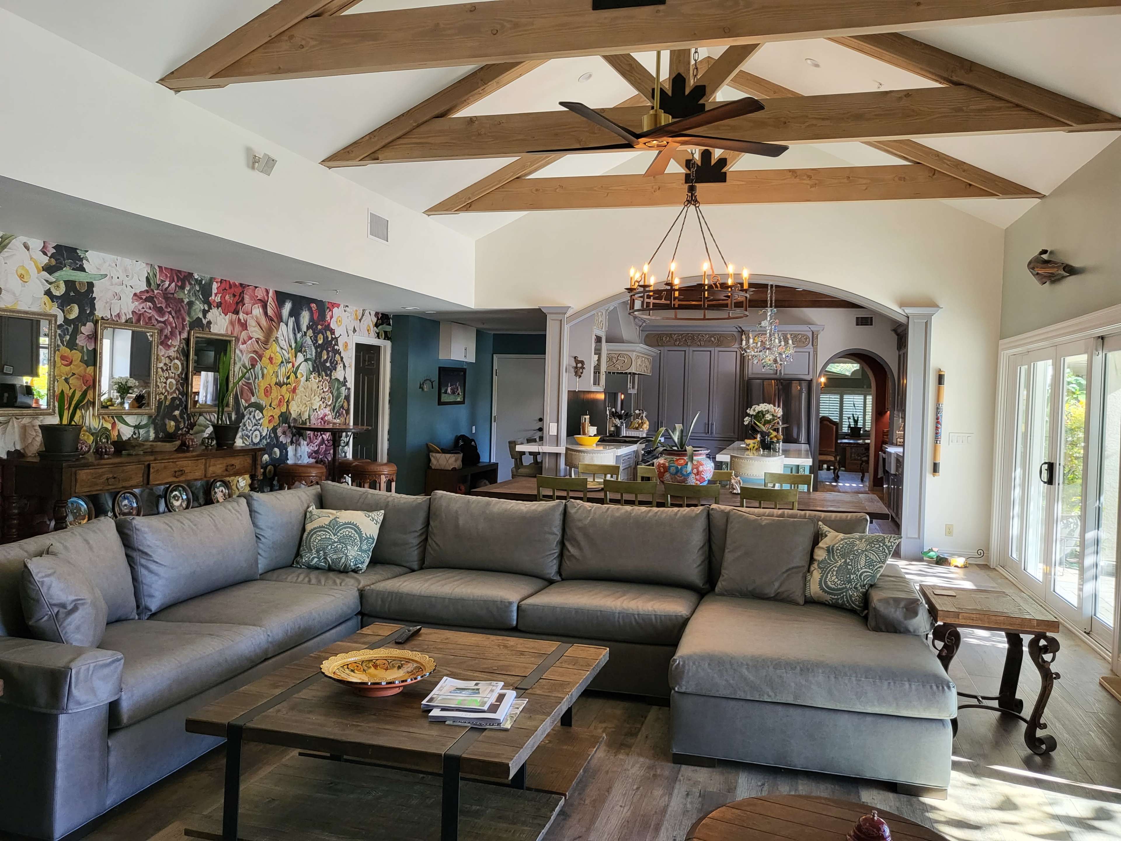 A spacious living room with a large sectional sofa, wooden beams on the ceiling, and an open layout that connects to a dining area in the background.