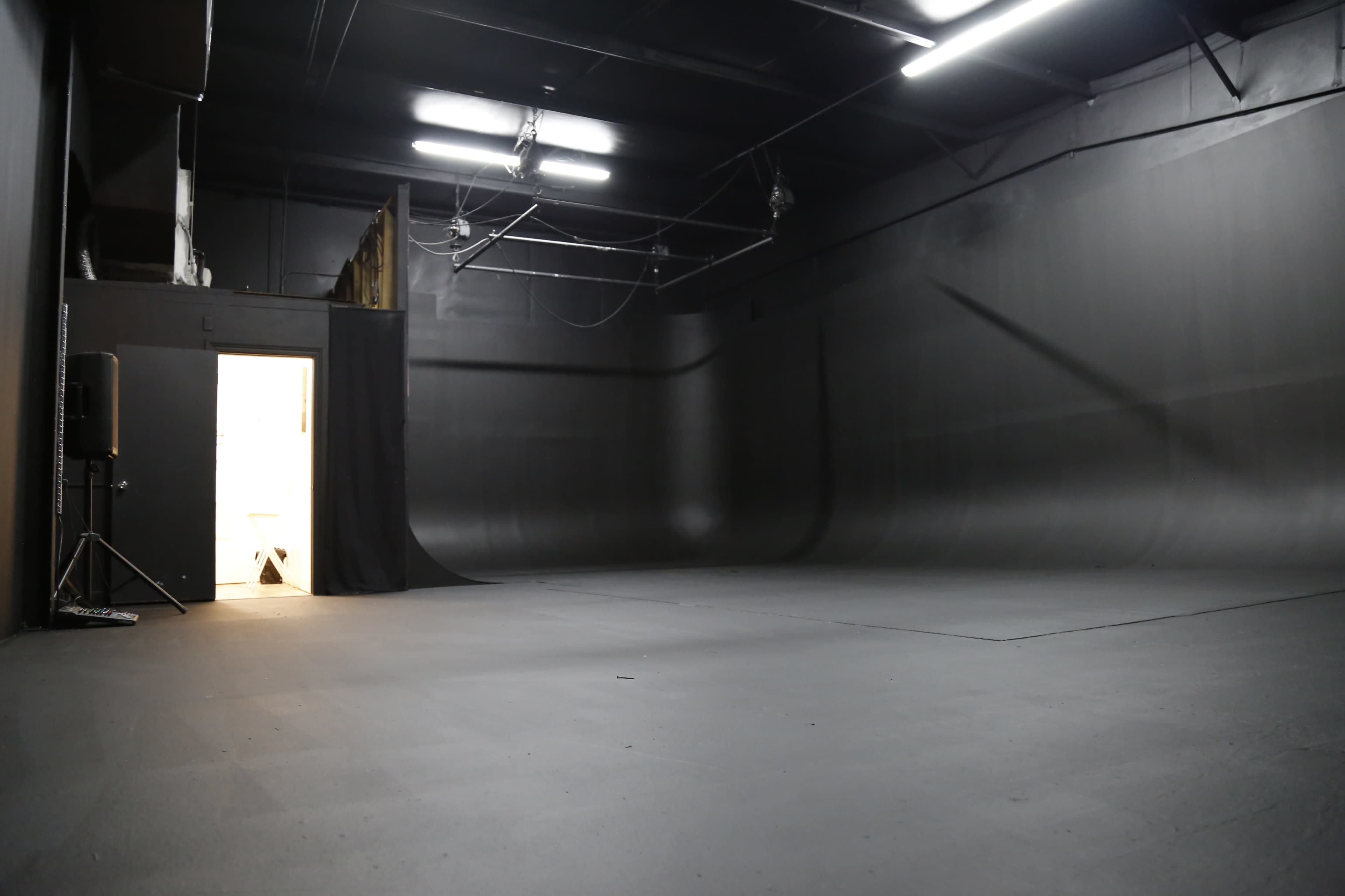 A large, empty black studio space with a door partially open at one end.