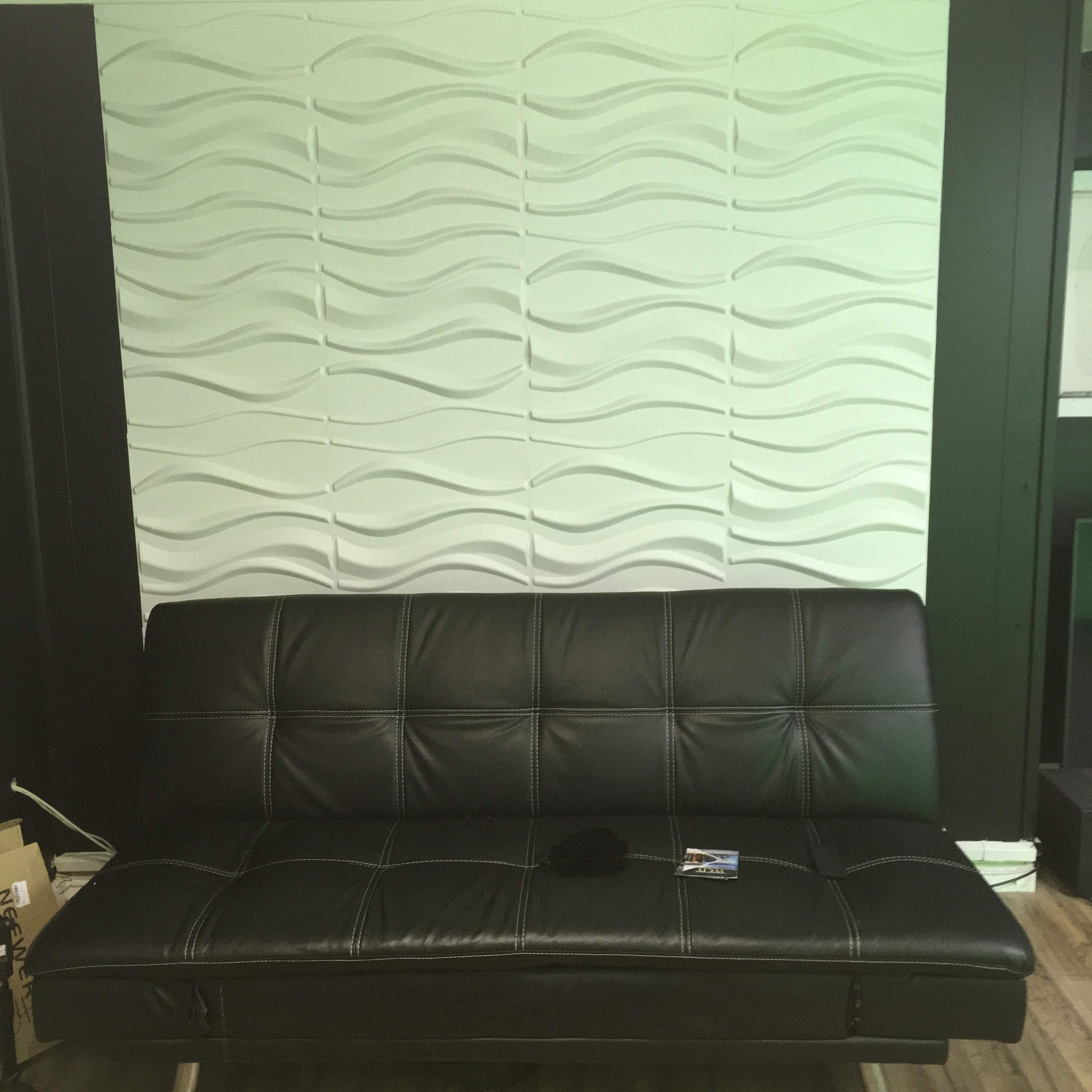 A black leather sofa is positioned against a textured wave-patterned wall.