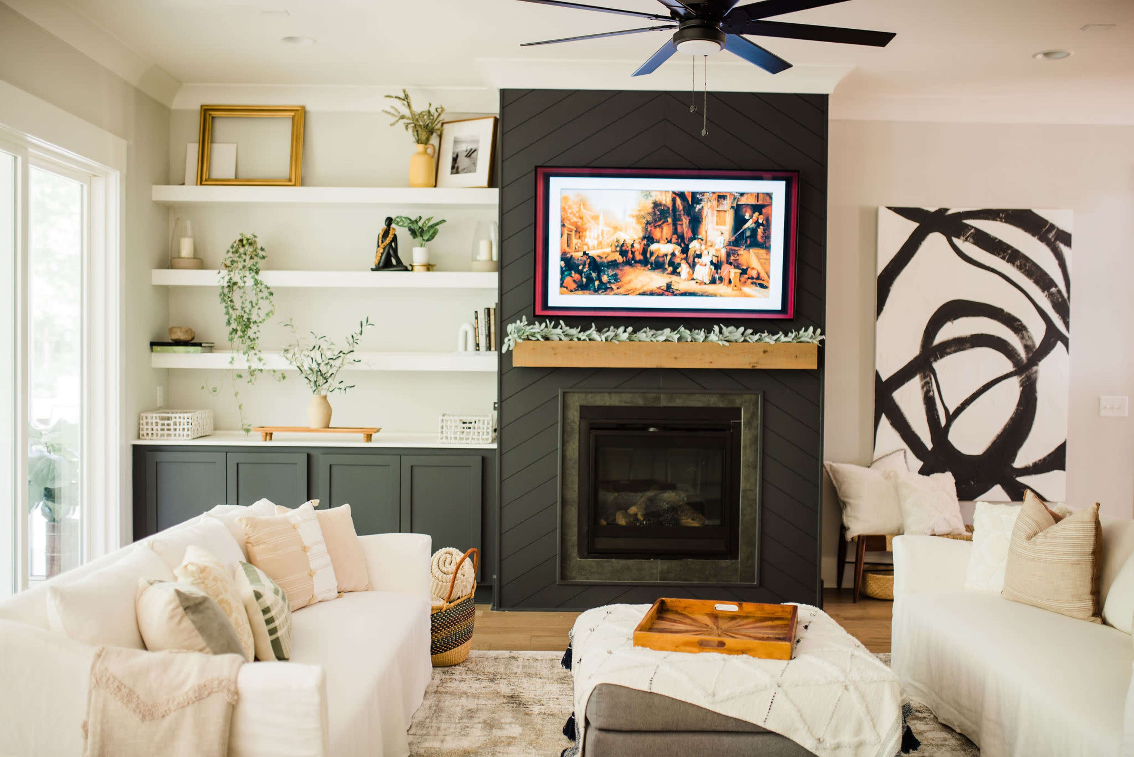 A modern living room features a dark accent wall with a mounted painting, a fireplace, and light-colored sofas arranged around a coffee table.