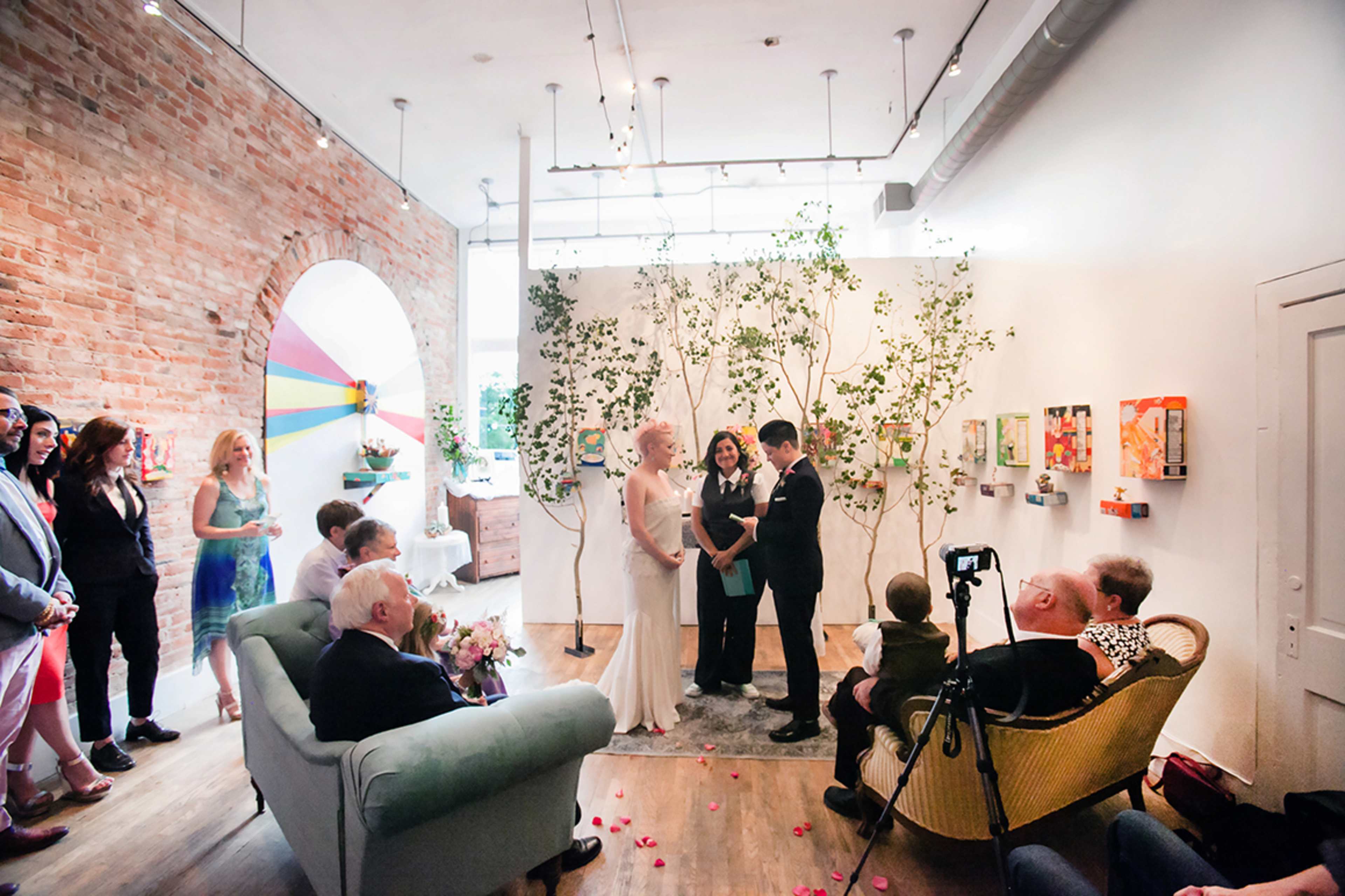 A couple stands in front of a small gathering of guests during a wedding ceremony in a decorated indoor setting.