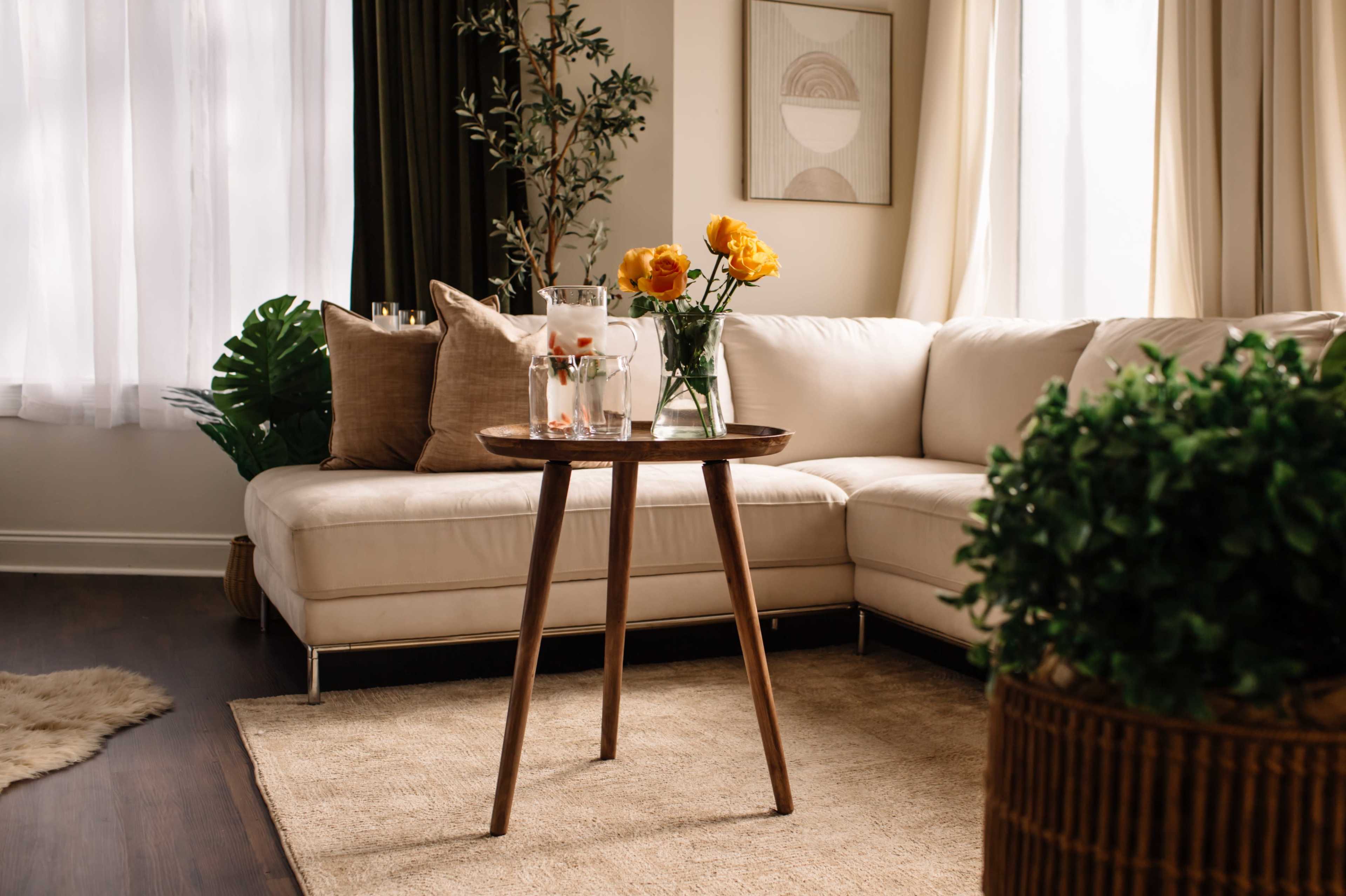 A cozy living room features a beige sectional sofa, a wooden side table with a vase of yellow flowers, and plants creating a warm atmosphere.