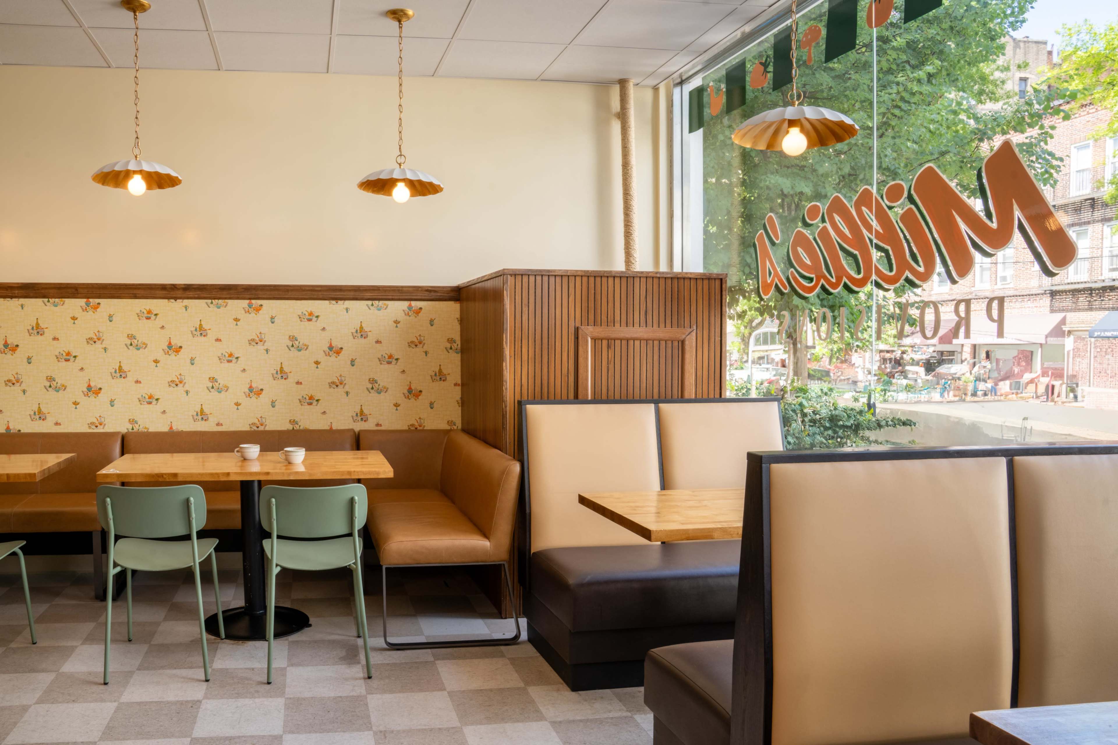 The image shows a cozy café interior with wooden tables, green chairs, and beige banquettes, illuminated by pendant lights.