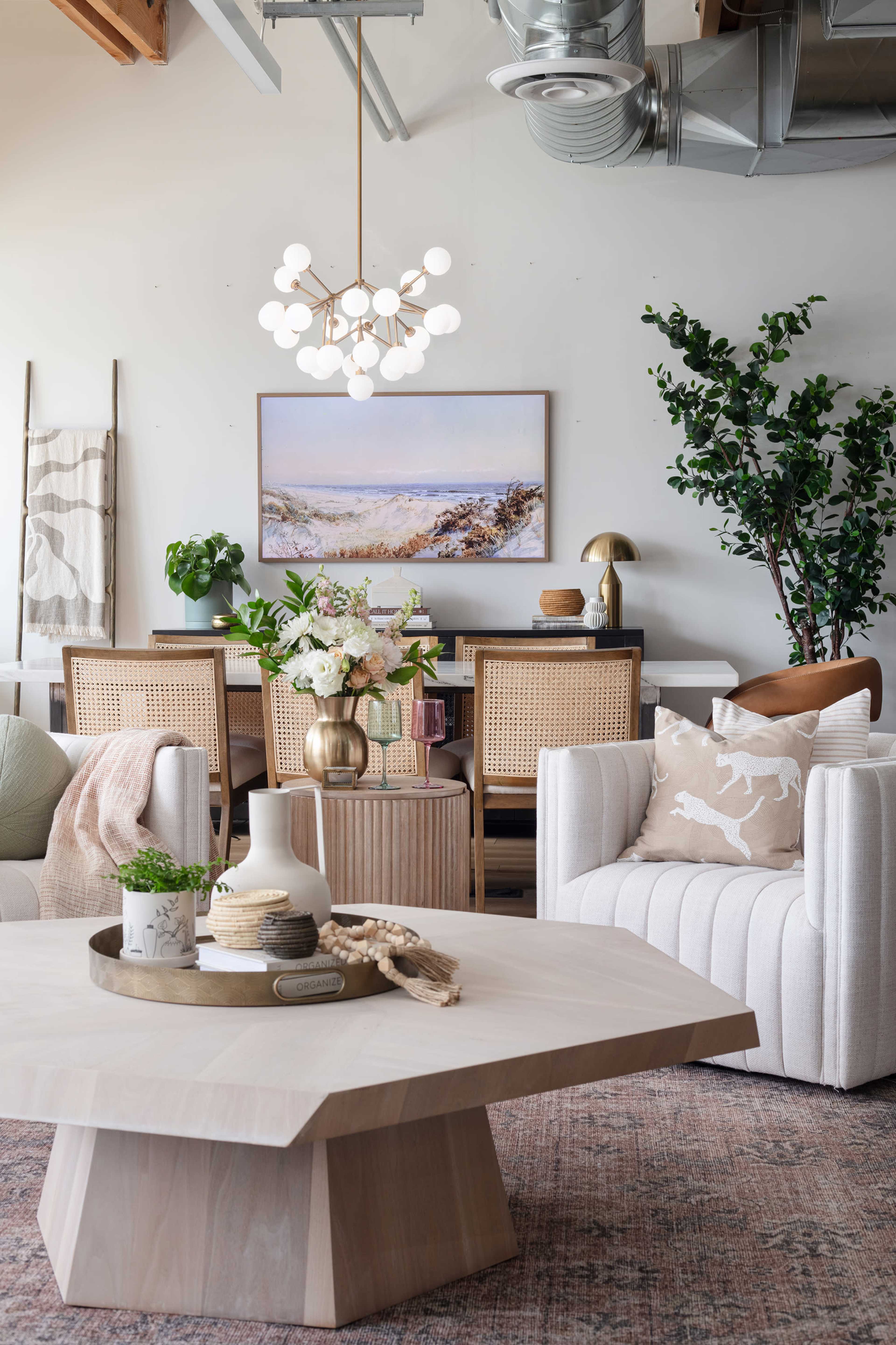 A modern living space features a light-filled room with a wooden coffee table, a dining area in the background, and decorative plants.