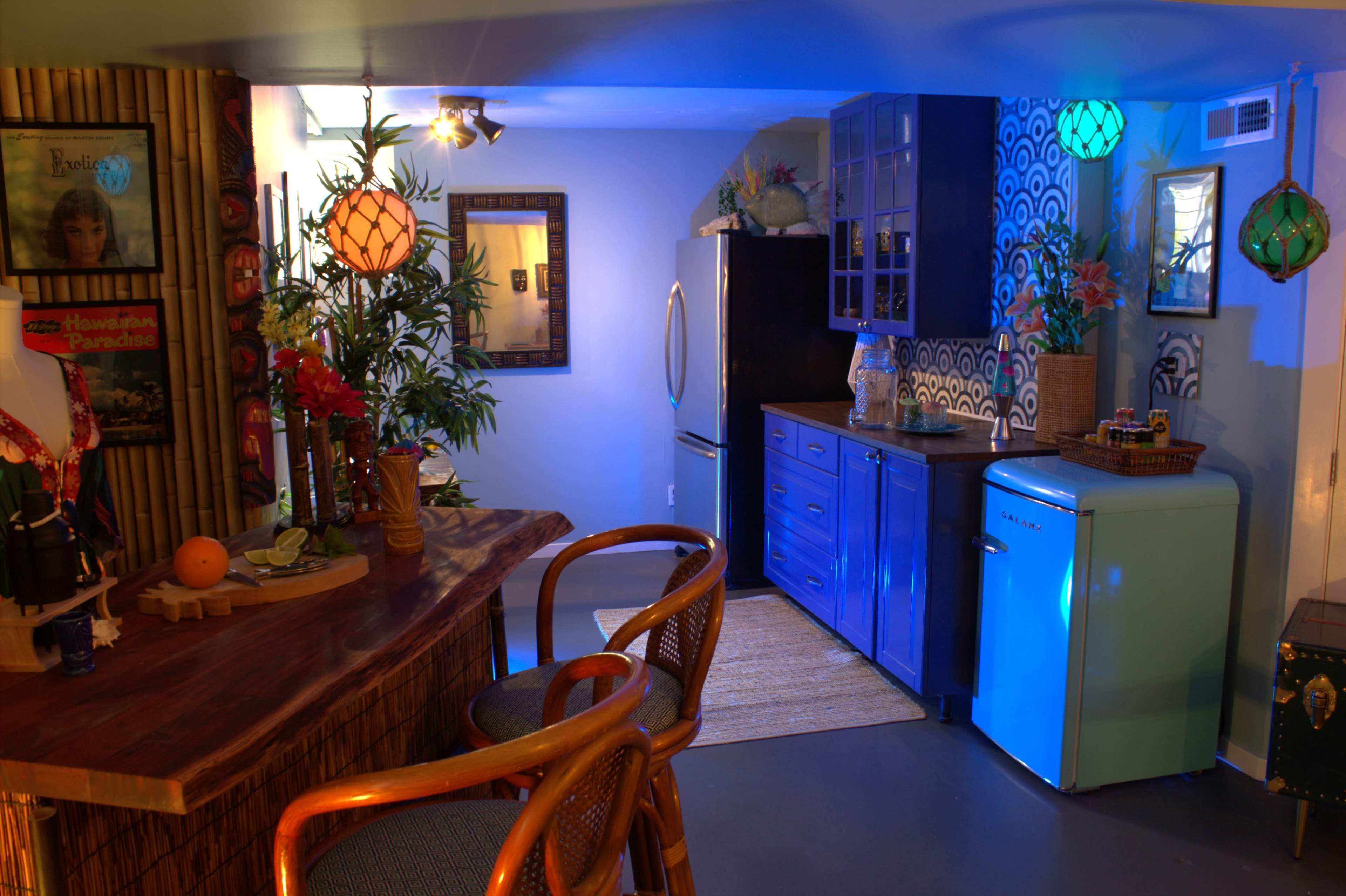 The image depicts a colorful kitchen with a blue refrigerator, wooden bar stools, and decorative lanterns providing ambient lighting.