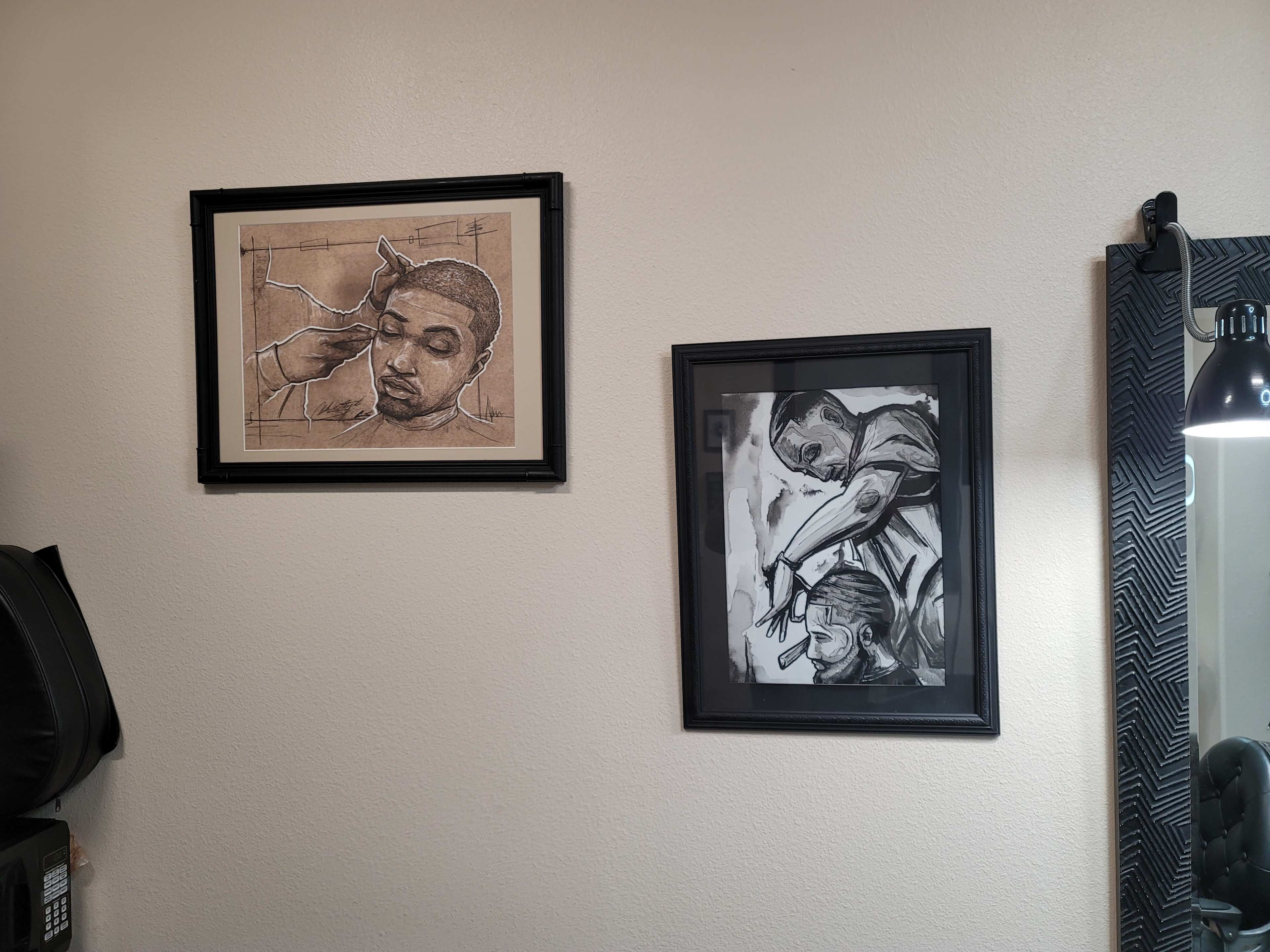 Two framed sketches of barbershop scenes mounted on a wall, with a mirror and a lamp visible in the corner.