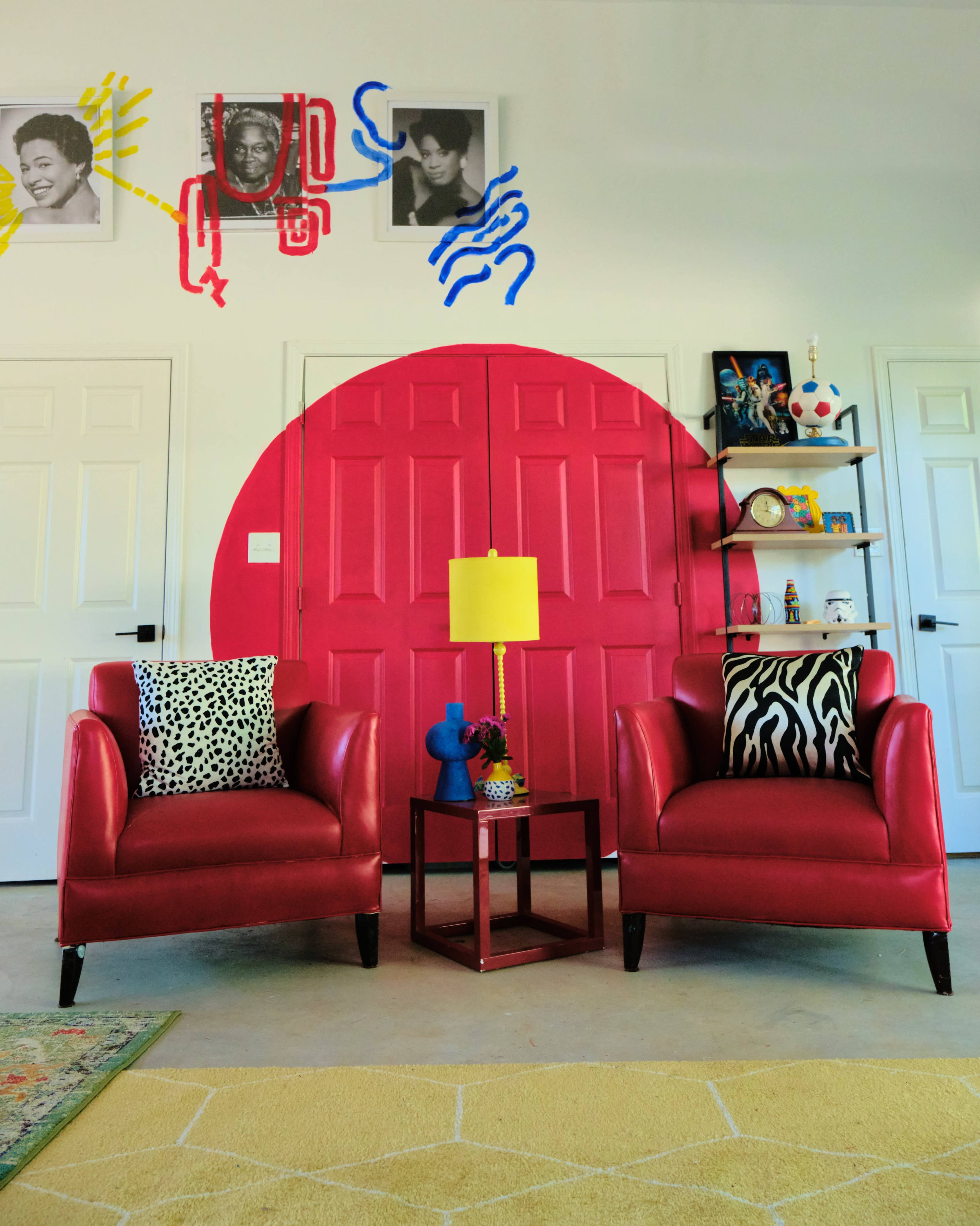 The image shows a modern living space with two red armchairs facing a bright pink circular wall, accompanied by a small table and decorative shelves.