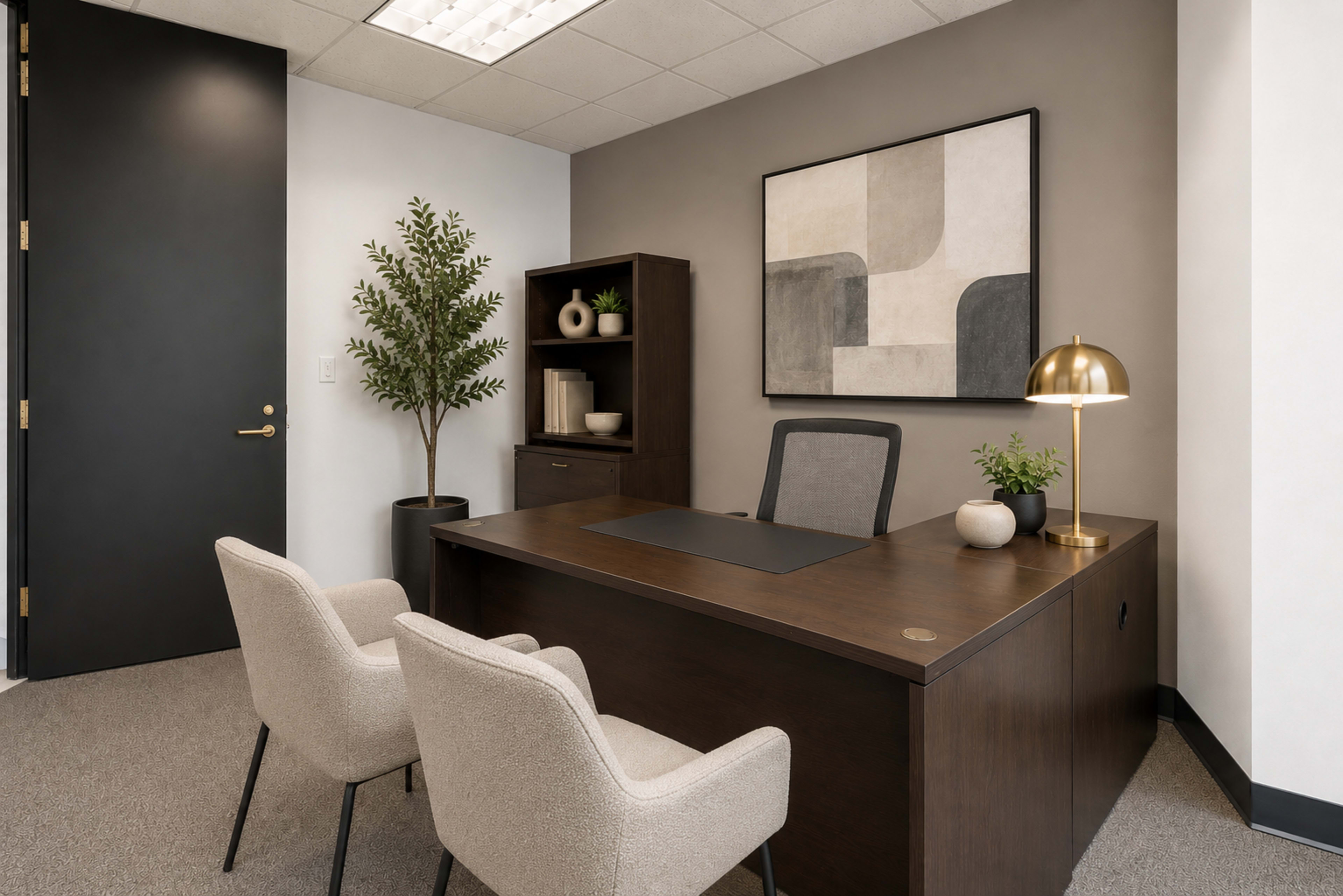 The image shows a modern office space featuring a wooden desk, two beige chairs, a bookshelf with decorative items, and a potted plant.