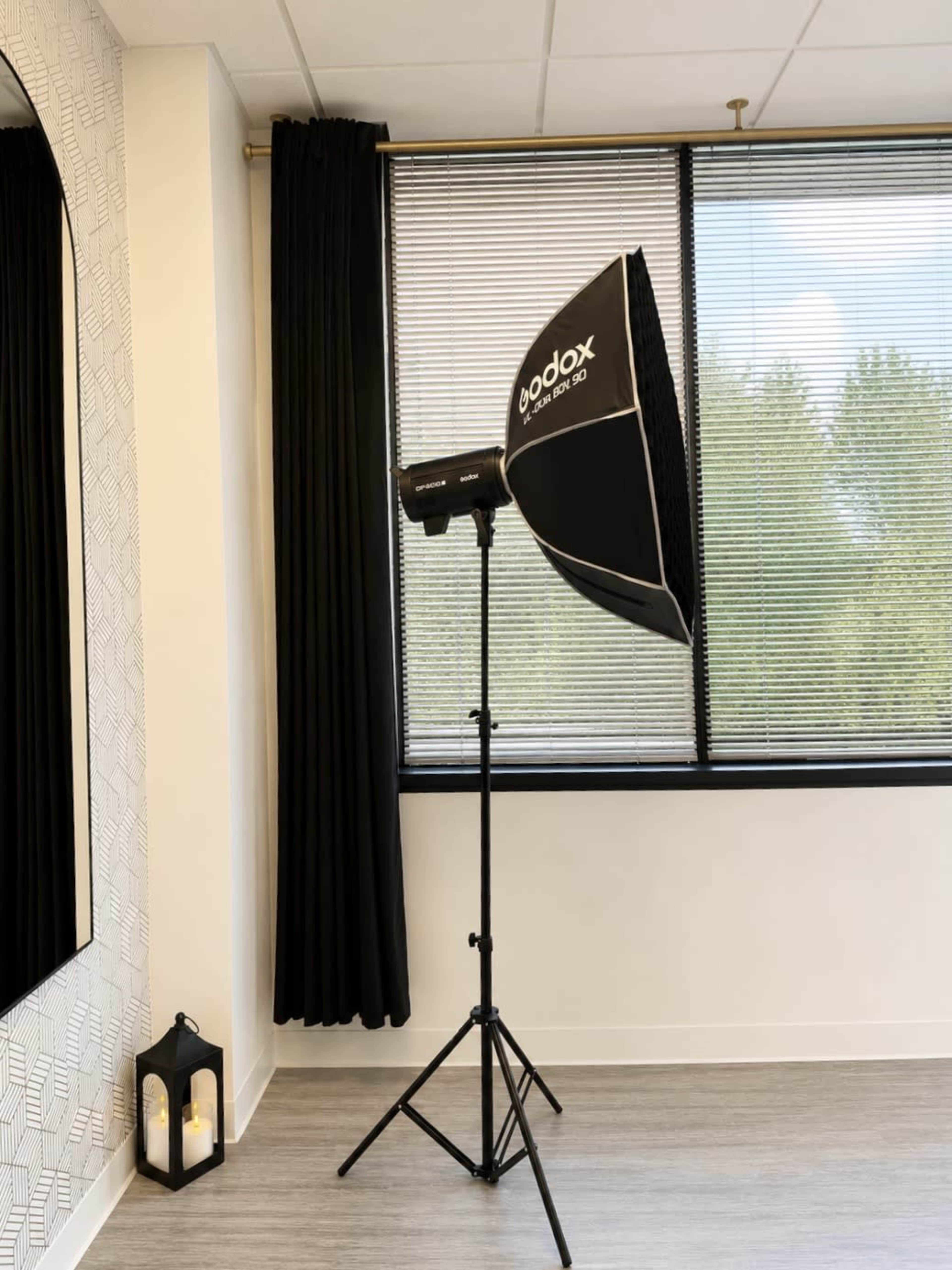 The image shows a Godox softbox light mounted on a stand near a window with closed blinds, alongside a decorative lantern on the floor.