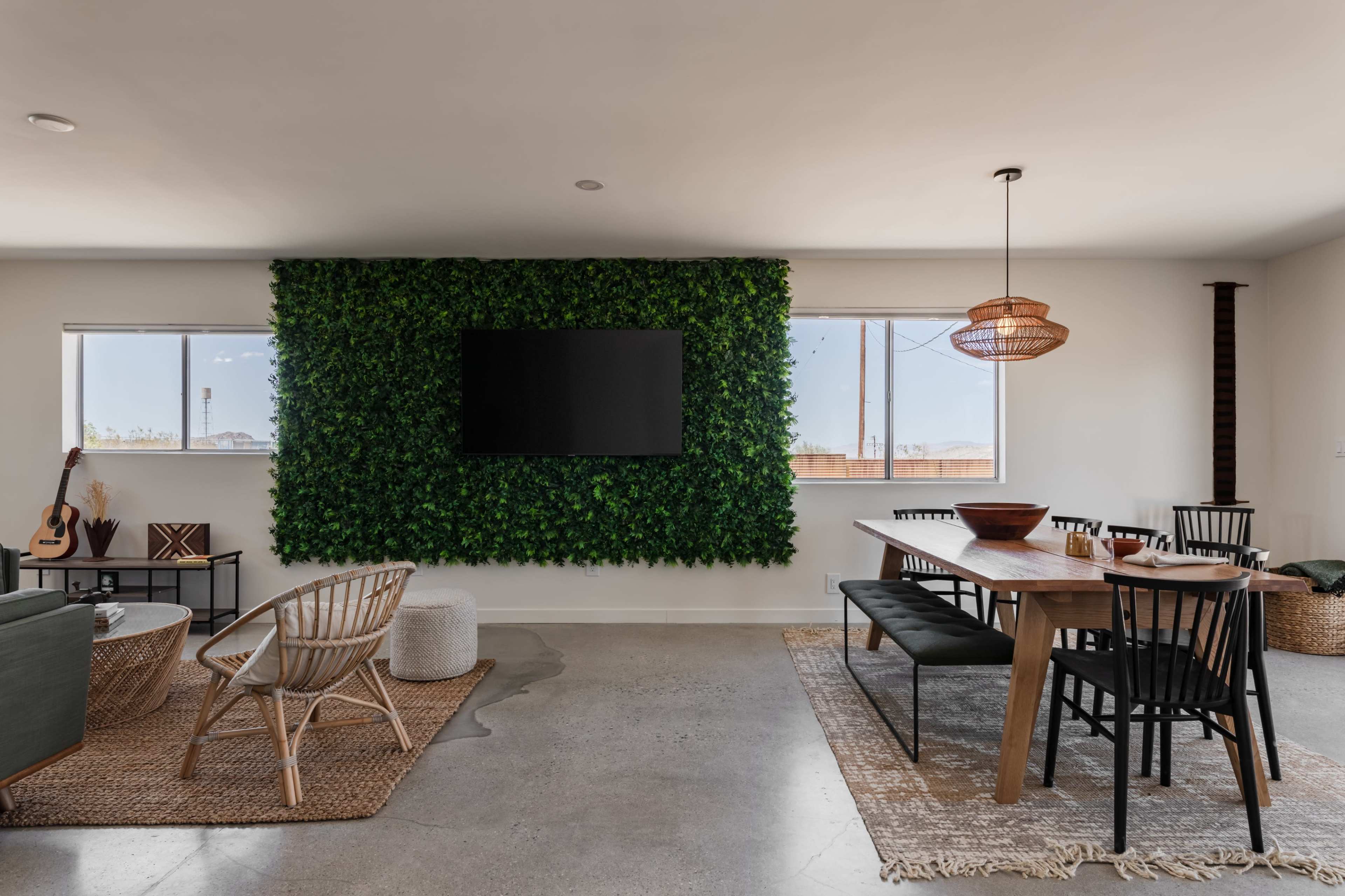 A modern living space features a wall of greenery, a television mounted above, and a dining area with a wooden table and black chairs.