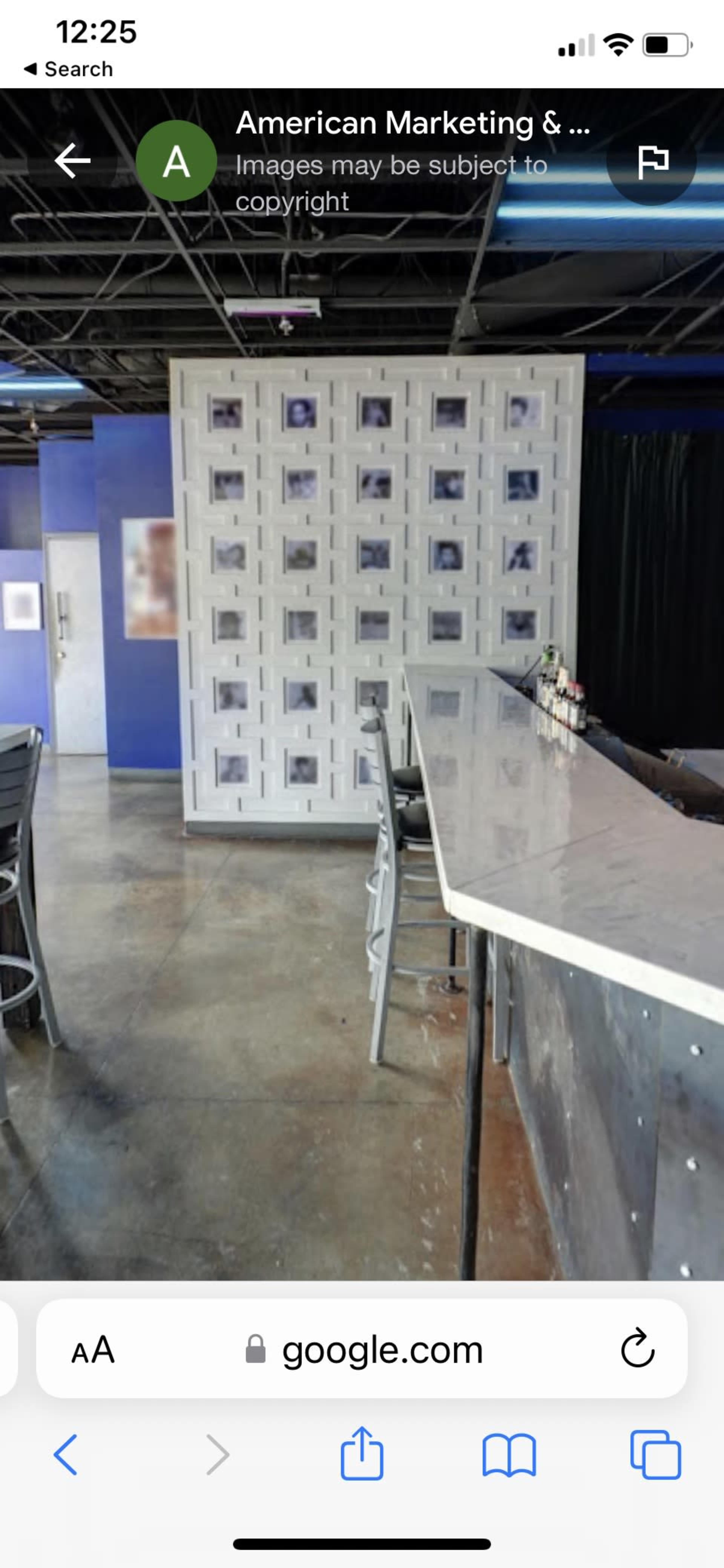 A modern bar area with a white countertop, silver accents, and a patterned wall featuring framed black and white photos.