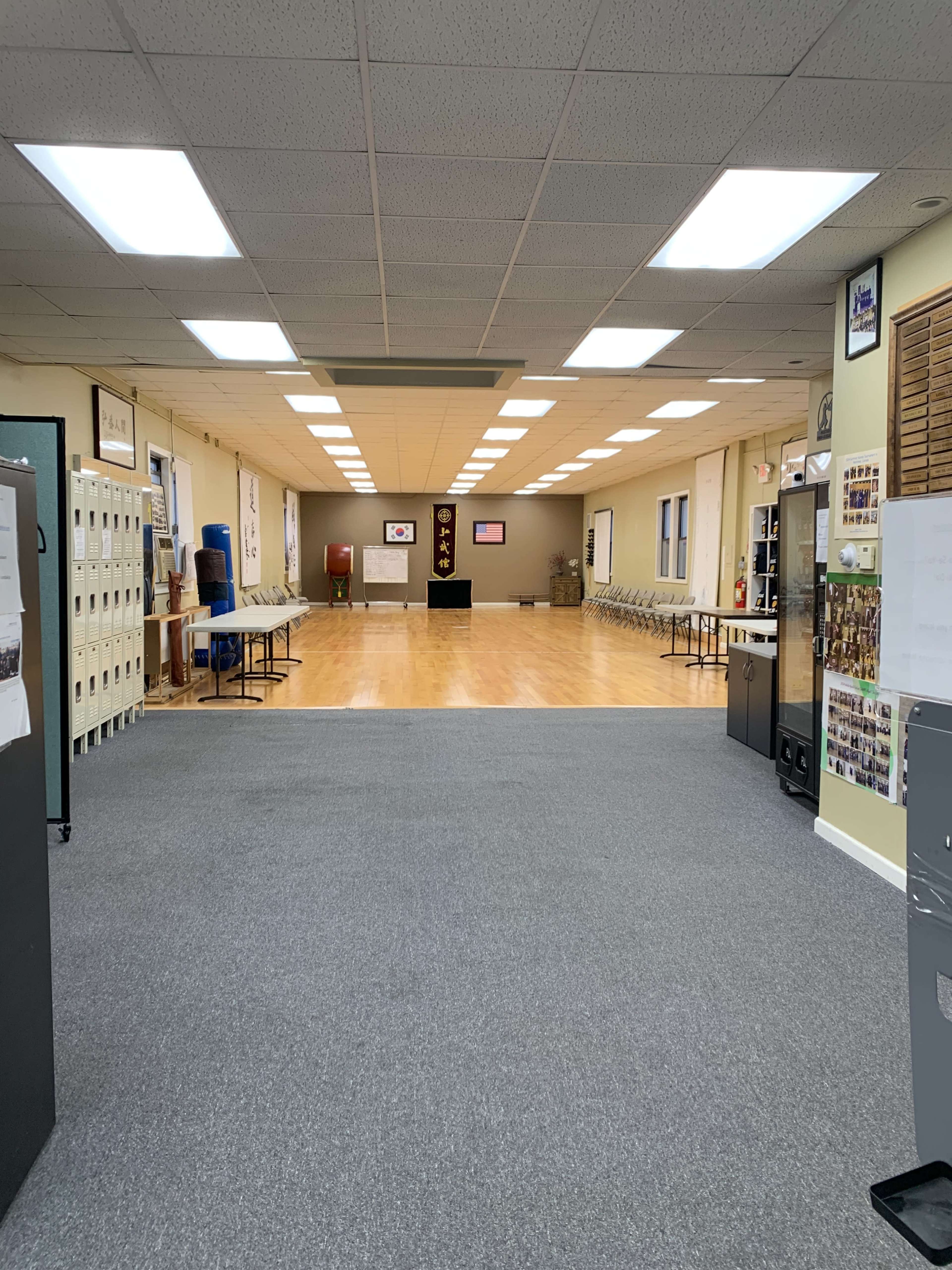 The image shows a spacious interior of a community hall or meeting room with chairs arranged in rows and a polished wooden floor.