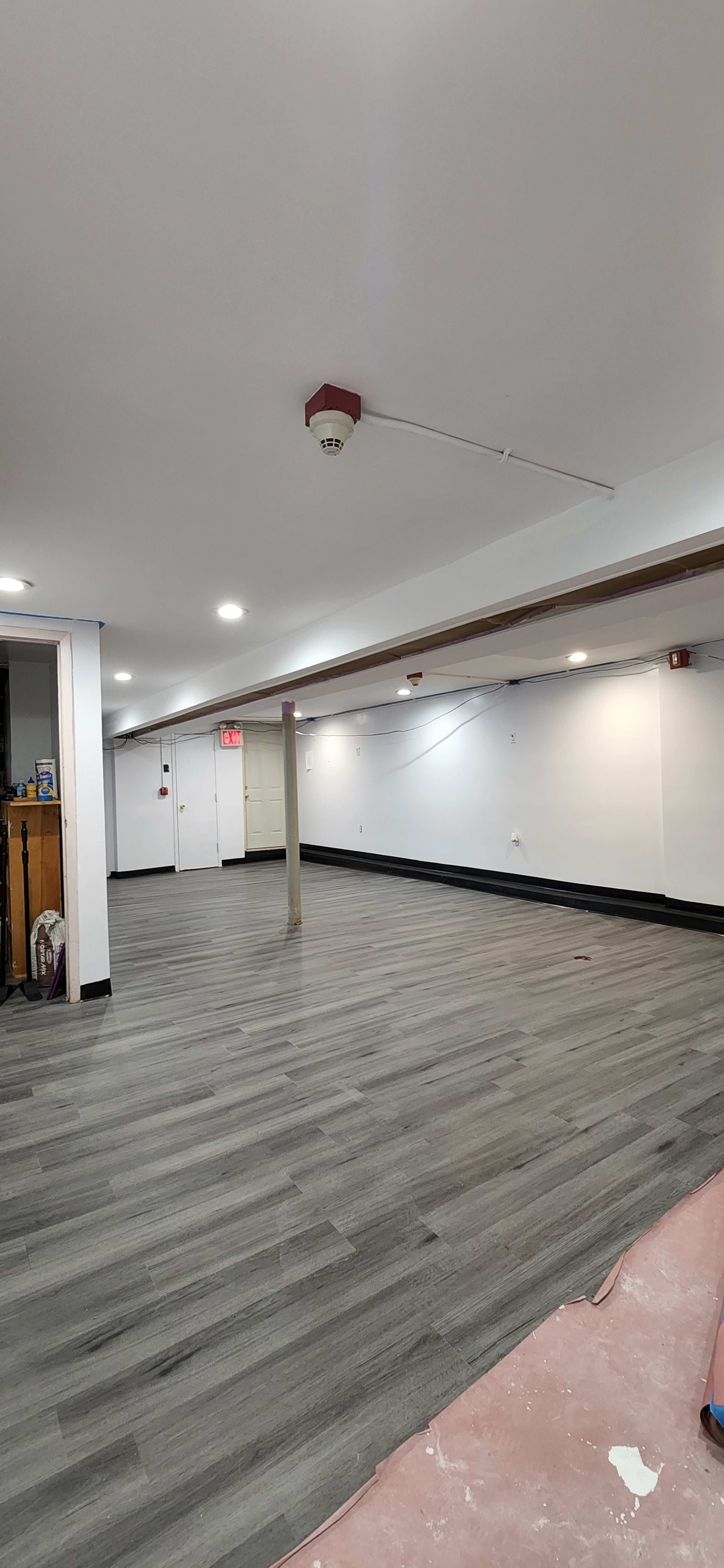 A spacious, empty basement room with gray wooden flooring and white walls.