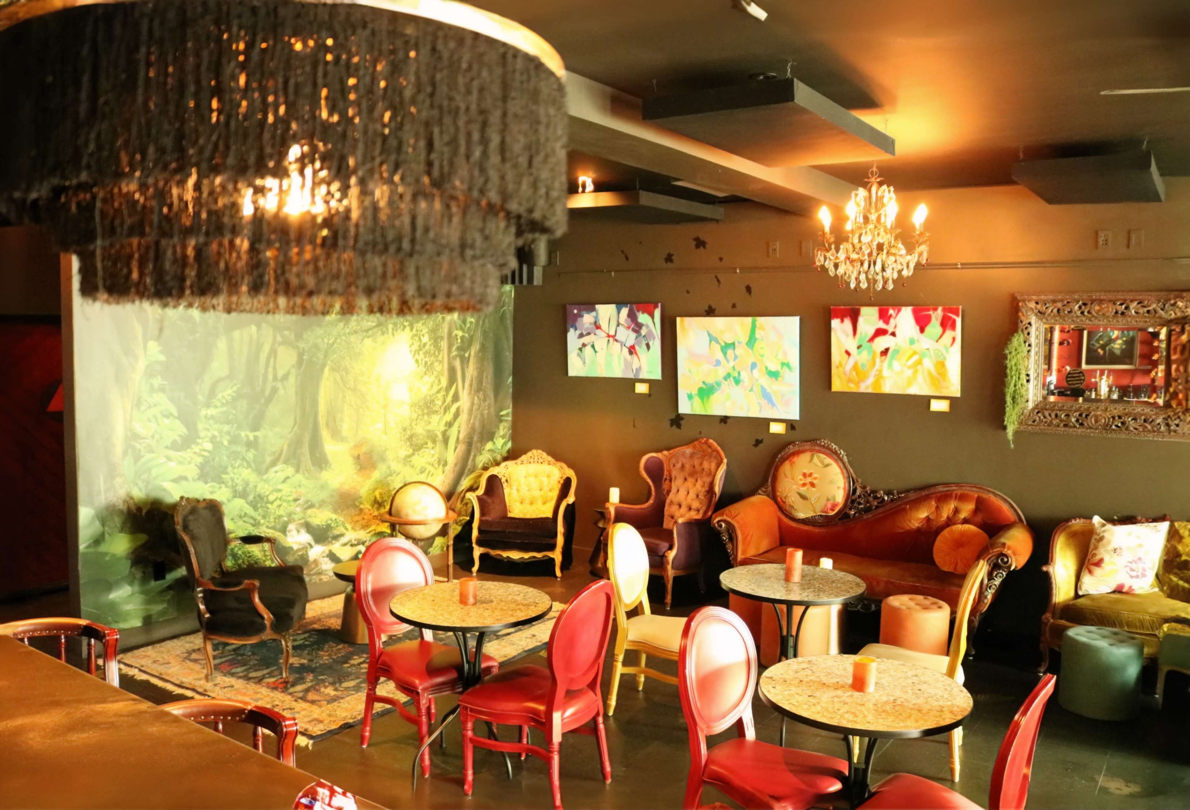 A cozy café interior with ornate seating, colorful artworks on the walls, and a scenic backdrop of a forest.