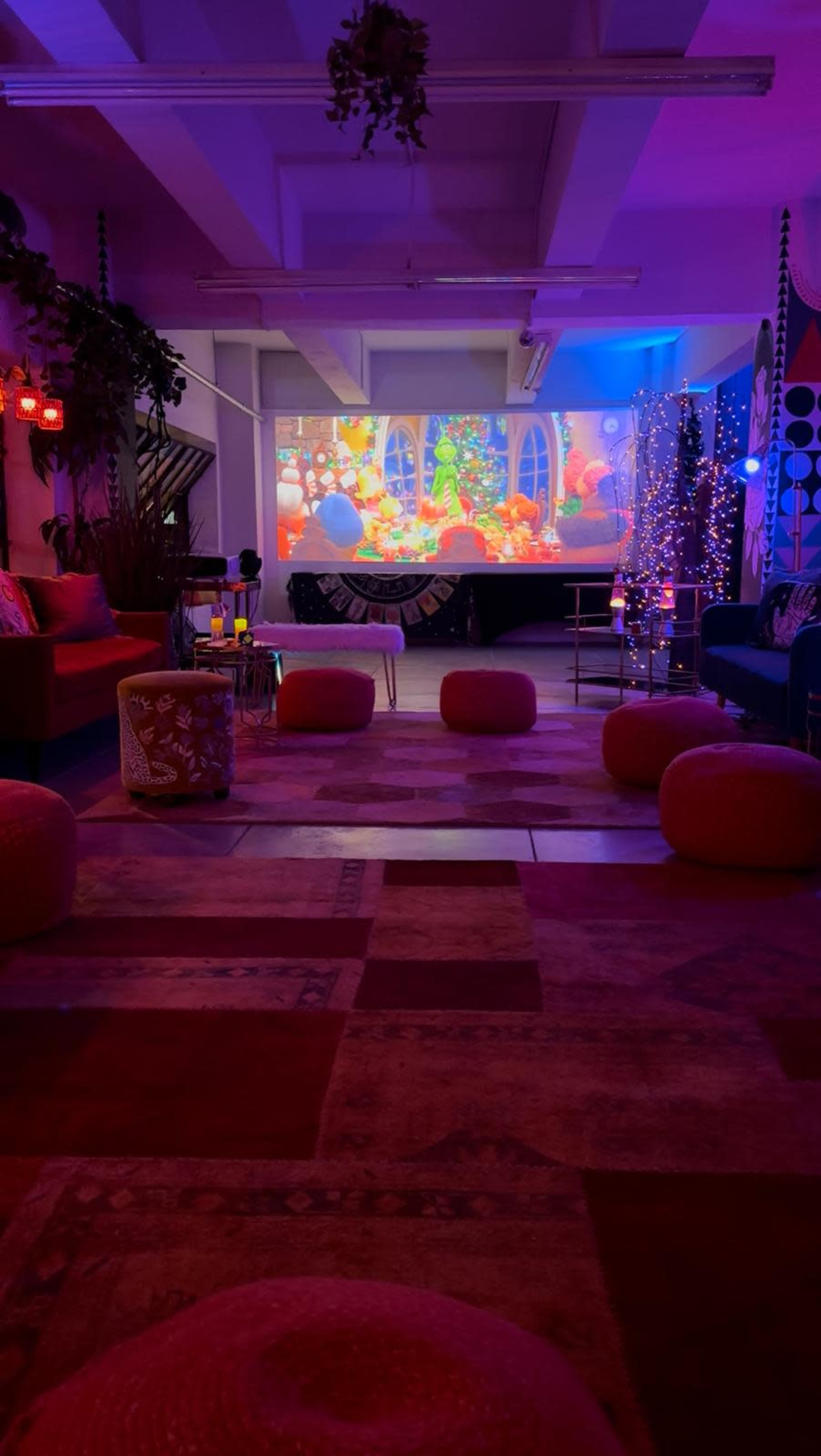 The image shows a cozy room with colorful seating, ambient lights, and a projector displaying vibrant animated visuals on a wall.