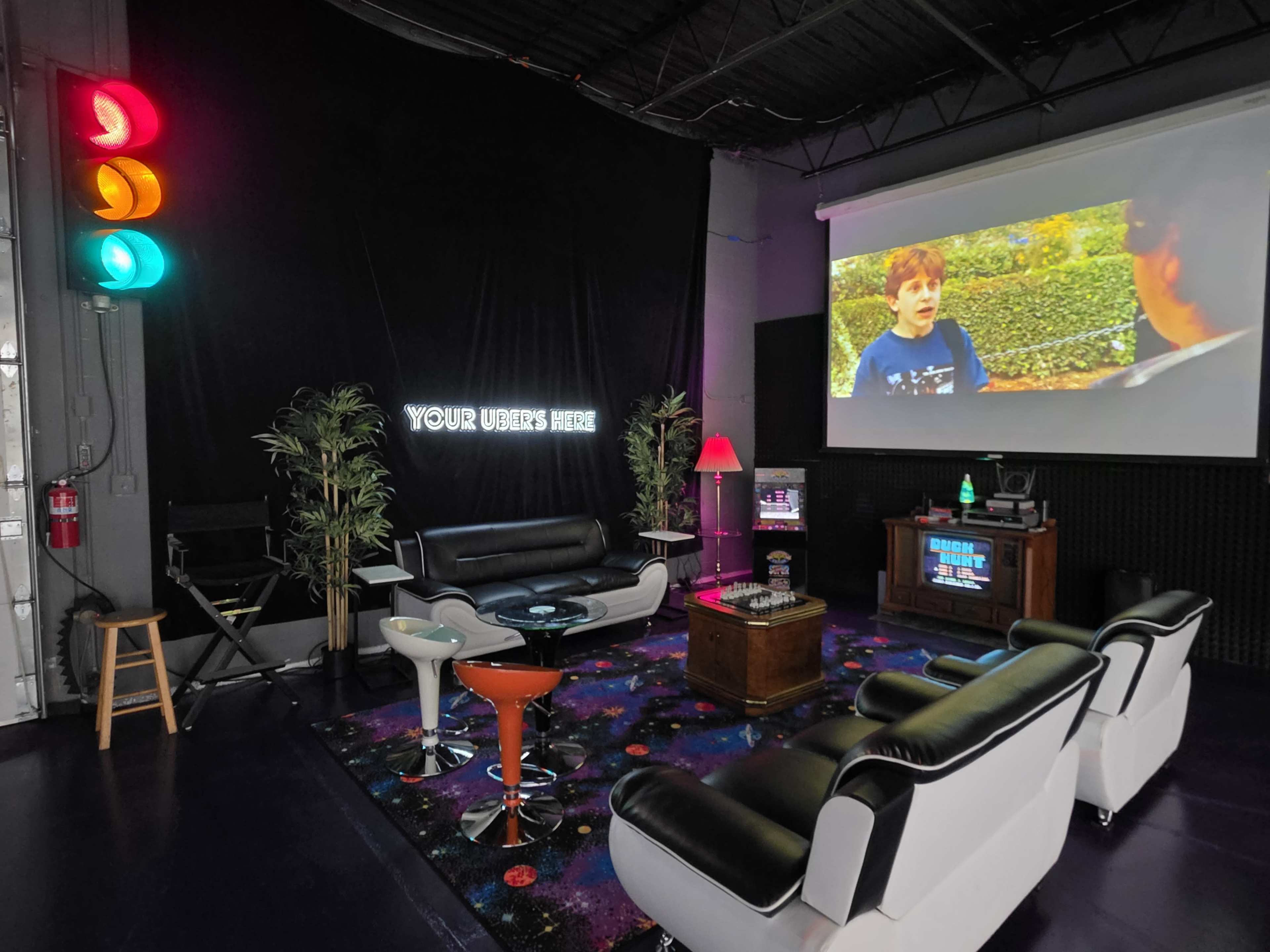 The image shows a modern lounge area featuring a projection screen, retro furniture, and a traffic light on the wall.