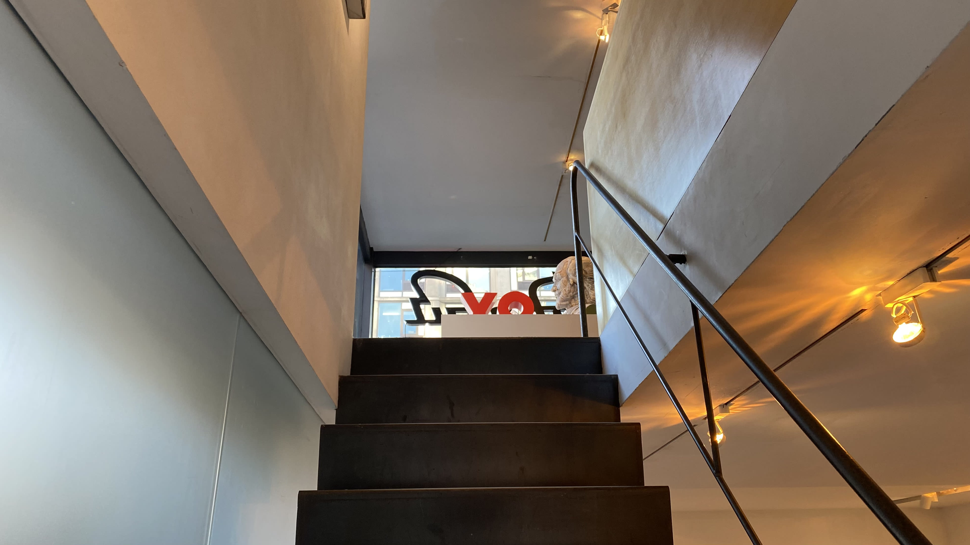 A staircase with black steps leads to a glass-enclosed area featuring a large red sculpture.