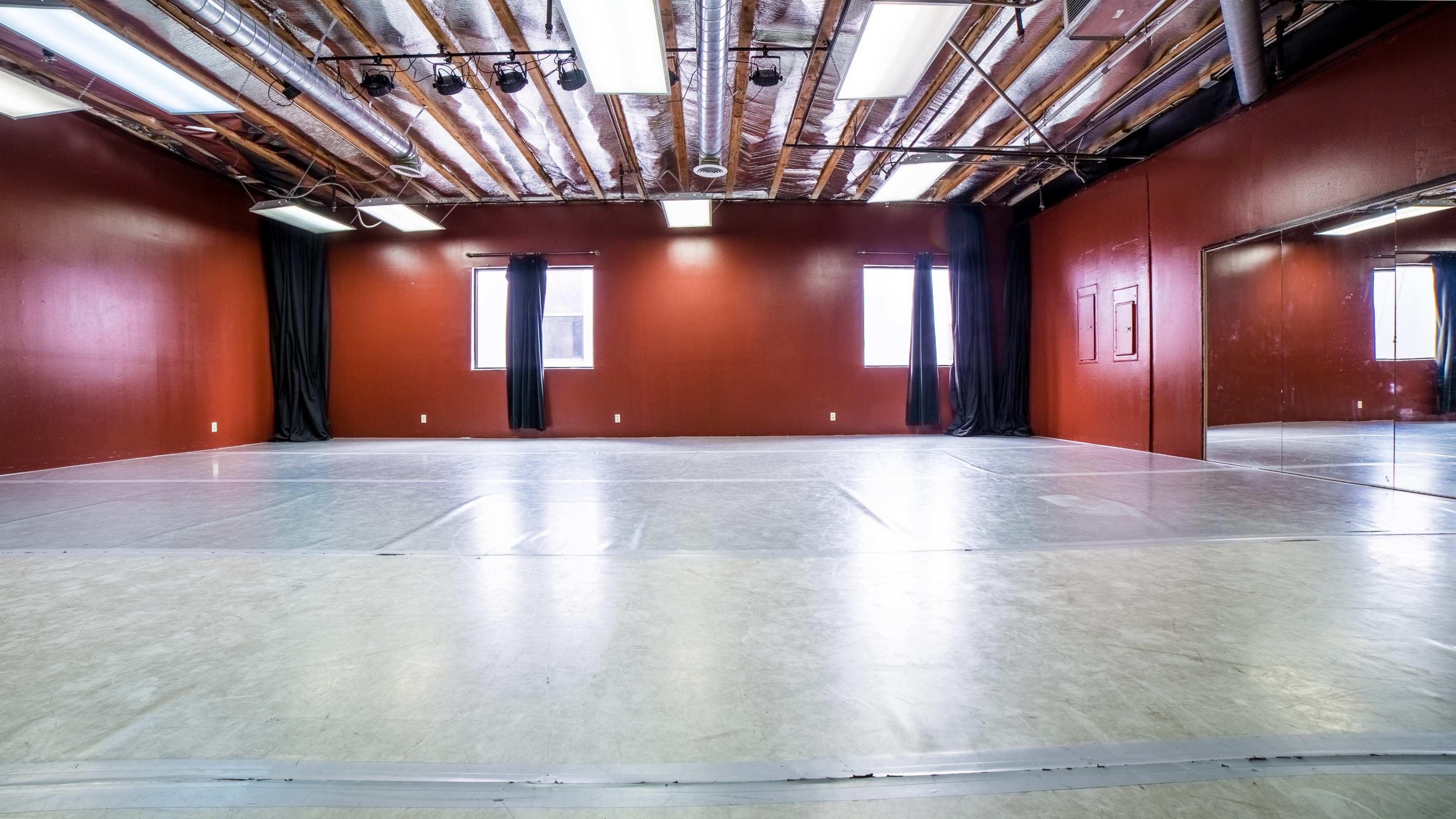 An empty dance studio with a wooden ceiling, red walls, and a mirrored wall.