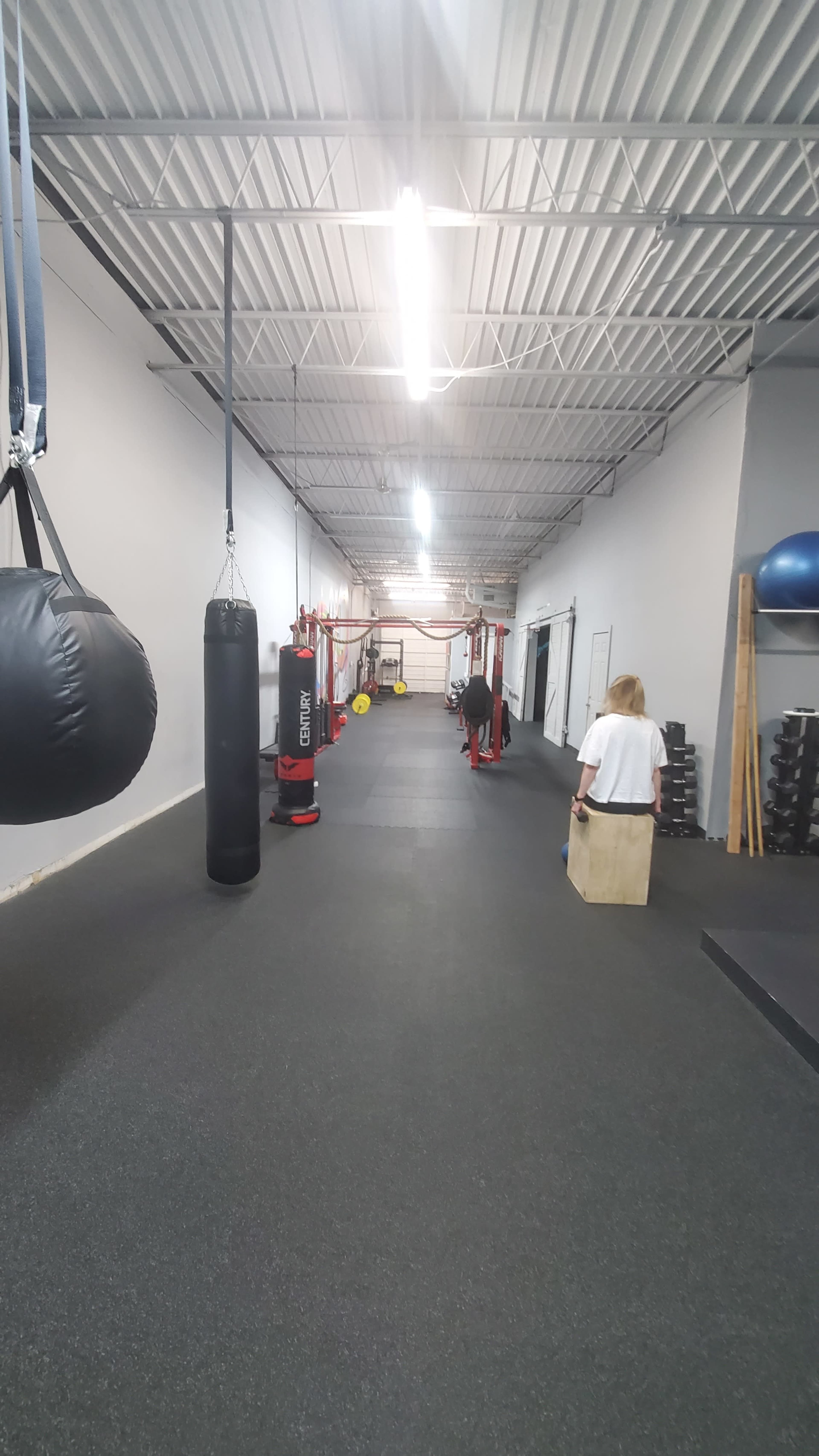 A long gym hallway filled with various workout equipment, including punching bags, weightlifting stations, and exercise balls.
