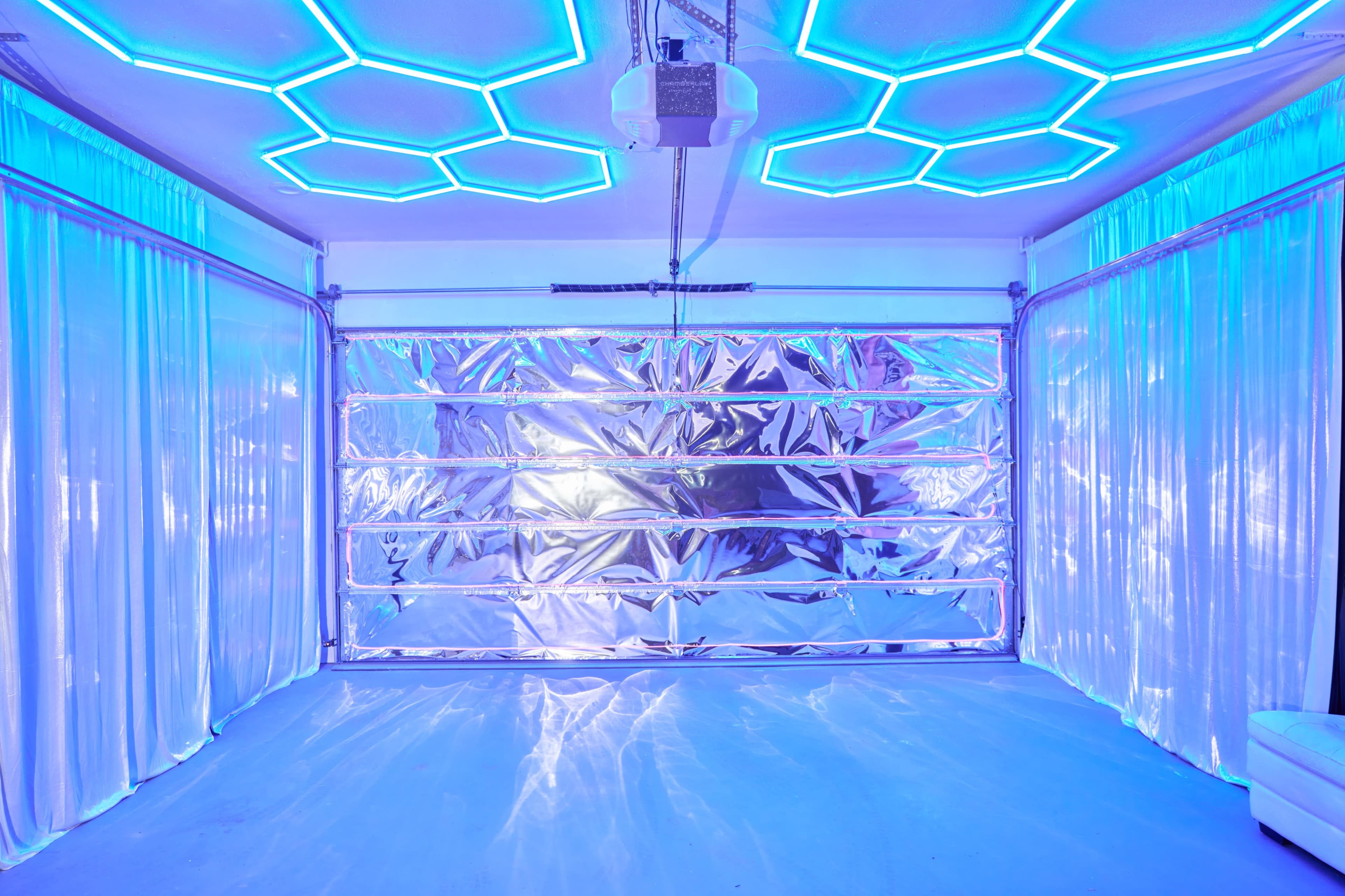 The image shows a modern garage with a shiny silver door and illuminated hexagonal ceiling lights casting a blue glow on the walls and floor.