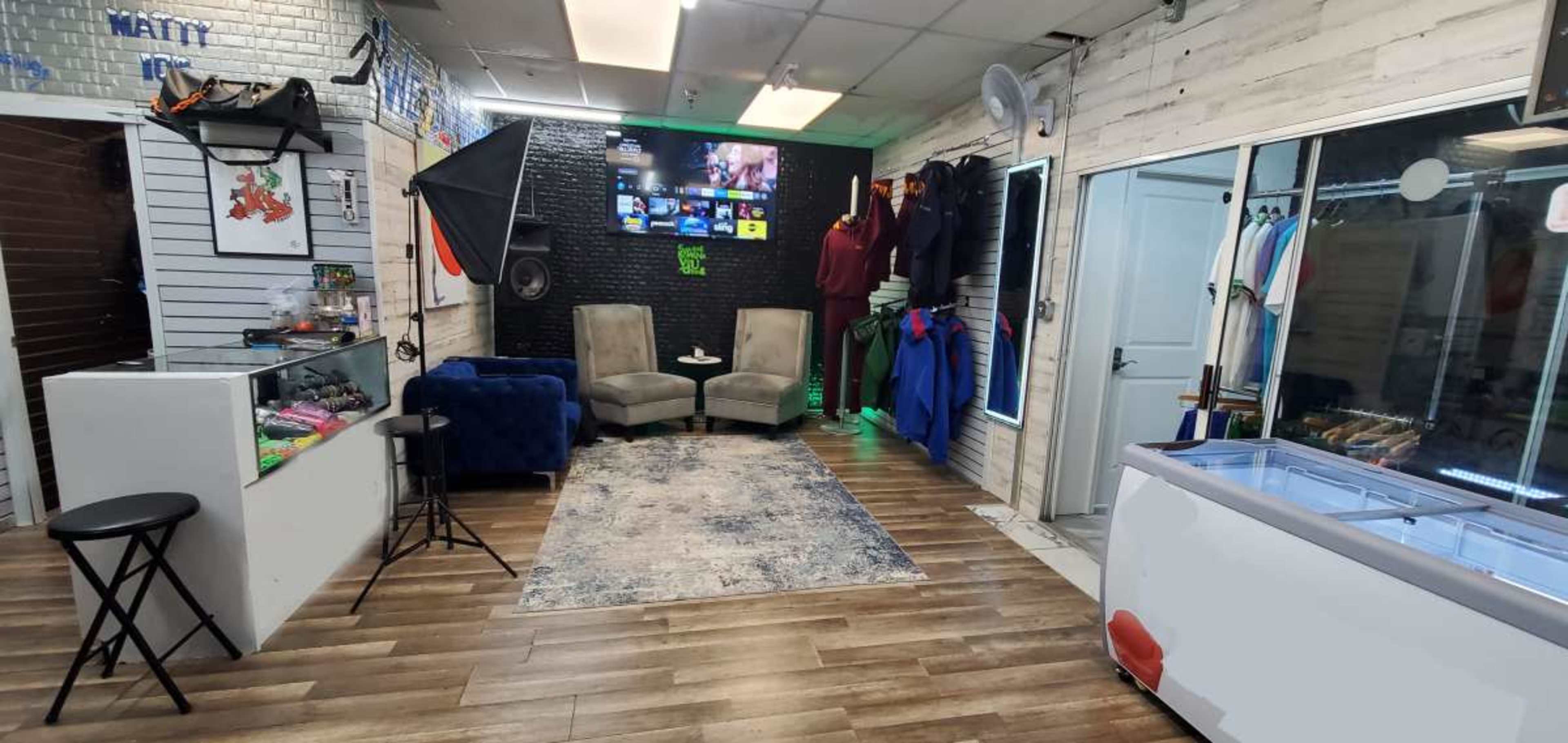 The image shows a retail space with two armchairs, a rug, and various clothing items displayed on racks along the walls.