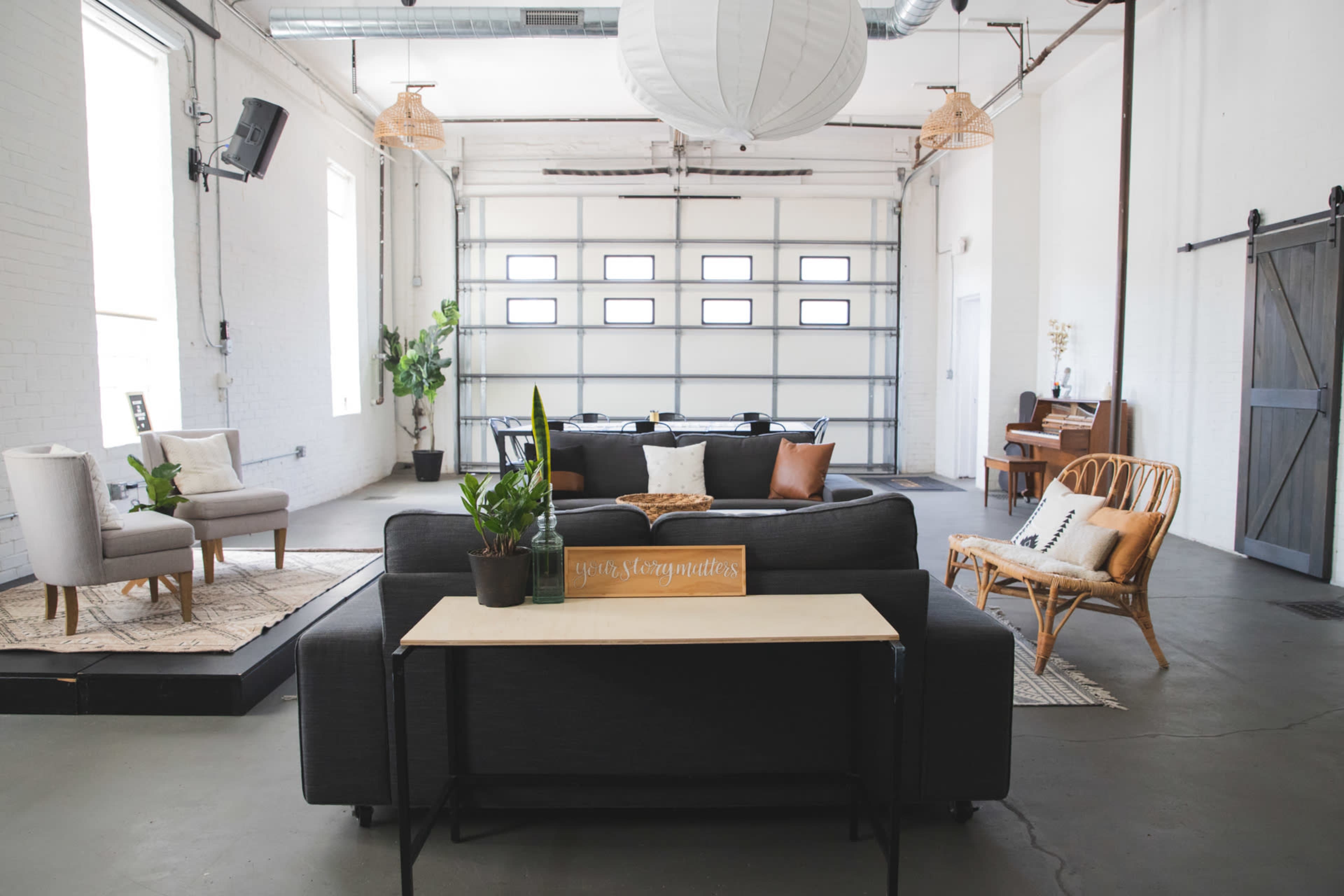 A spacious, minimalist living area with modern furniture, a large garage door, and a piano in the background.