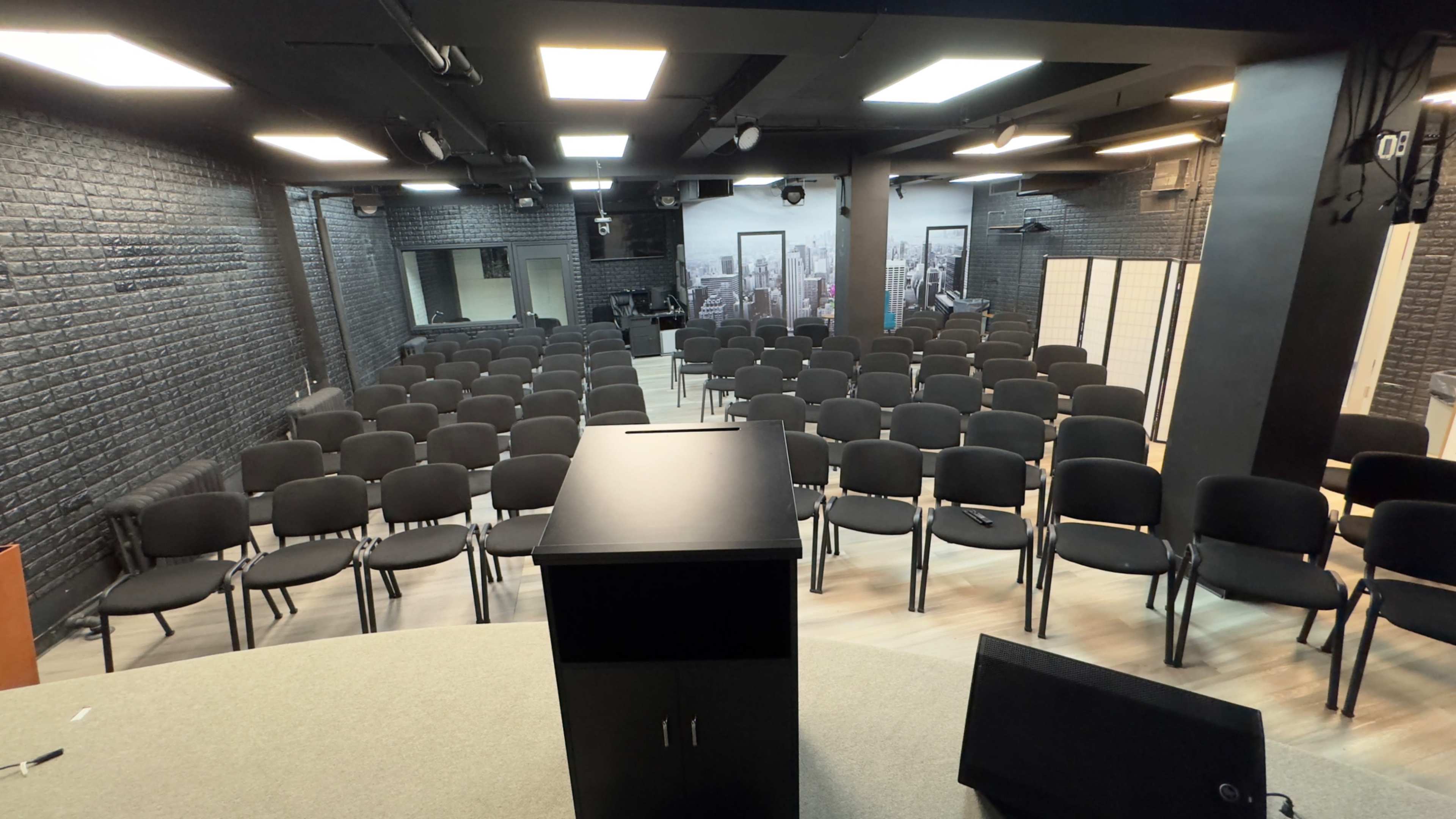 A conference room arranged with rows of black chairs facing a black podium on a circular stage.